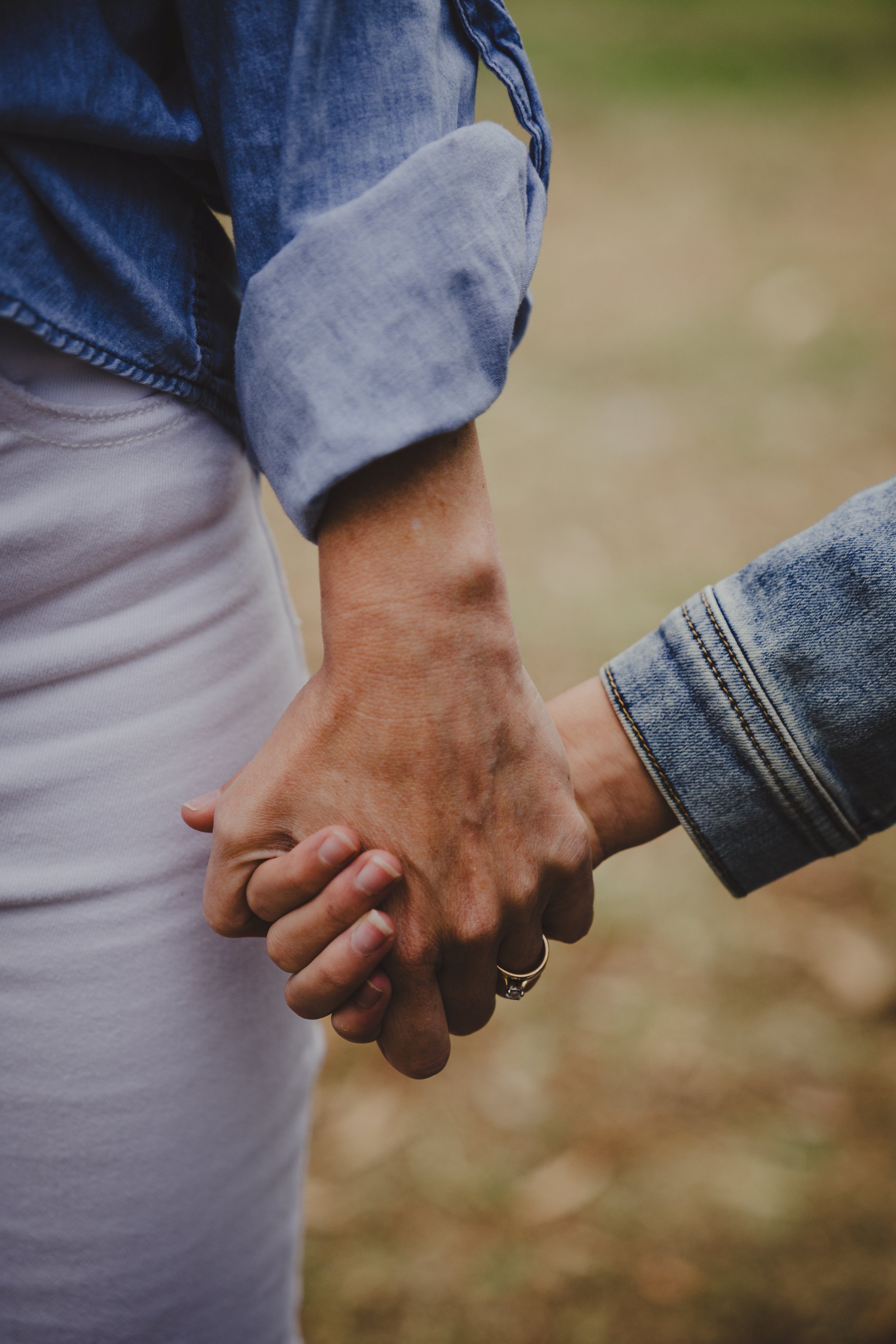Close-up of two people holding hands, with one person wearing a blue denim jacket and light-colored pants, and the other person also wearing a denim jacket.