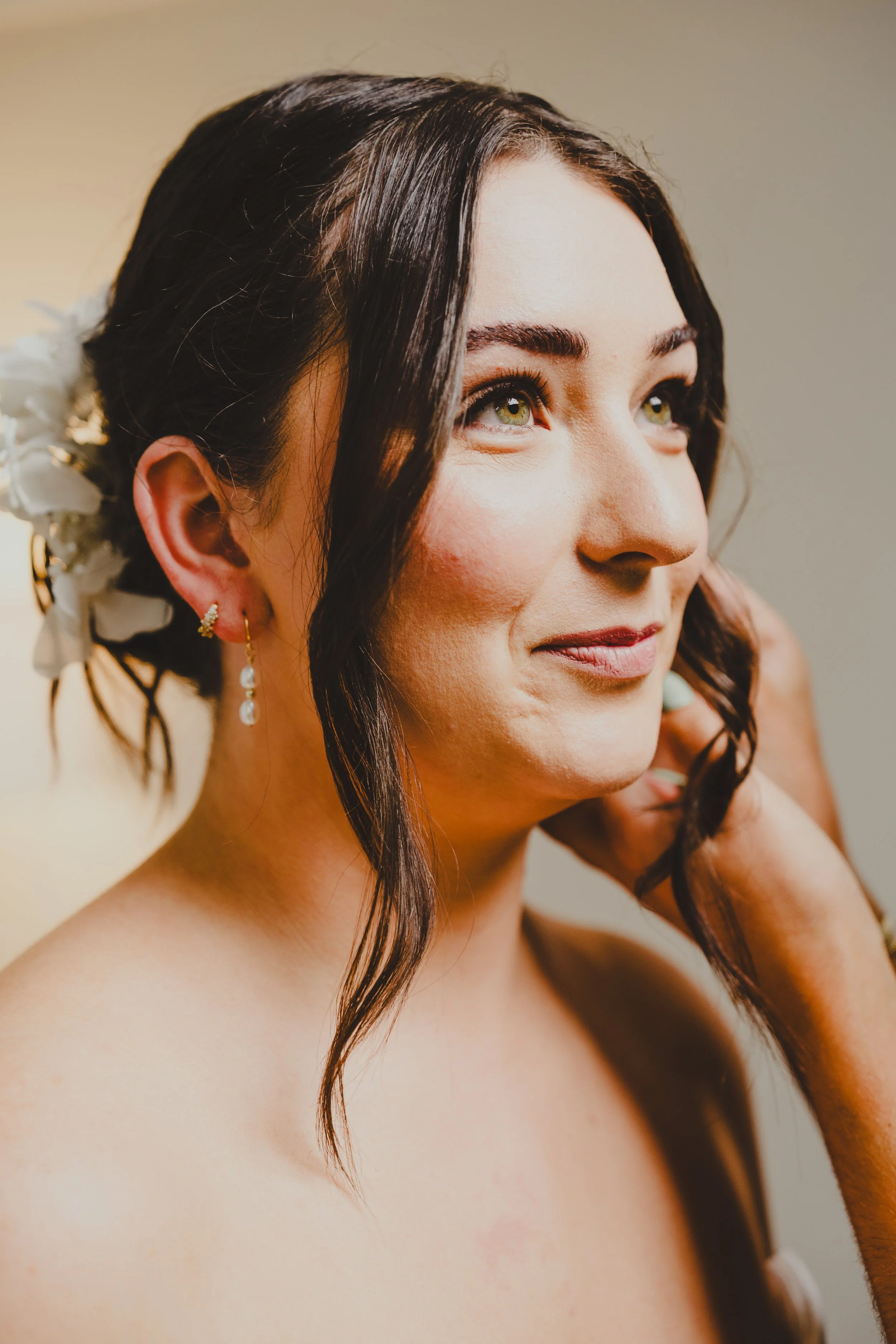 Close-up of a woman with dark hair, jewelry, and floral accessories adjusting her earring.