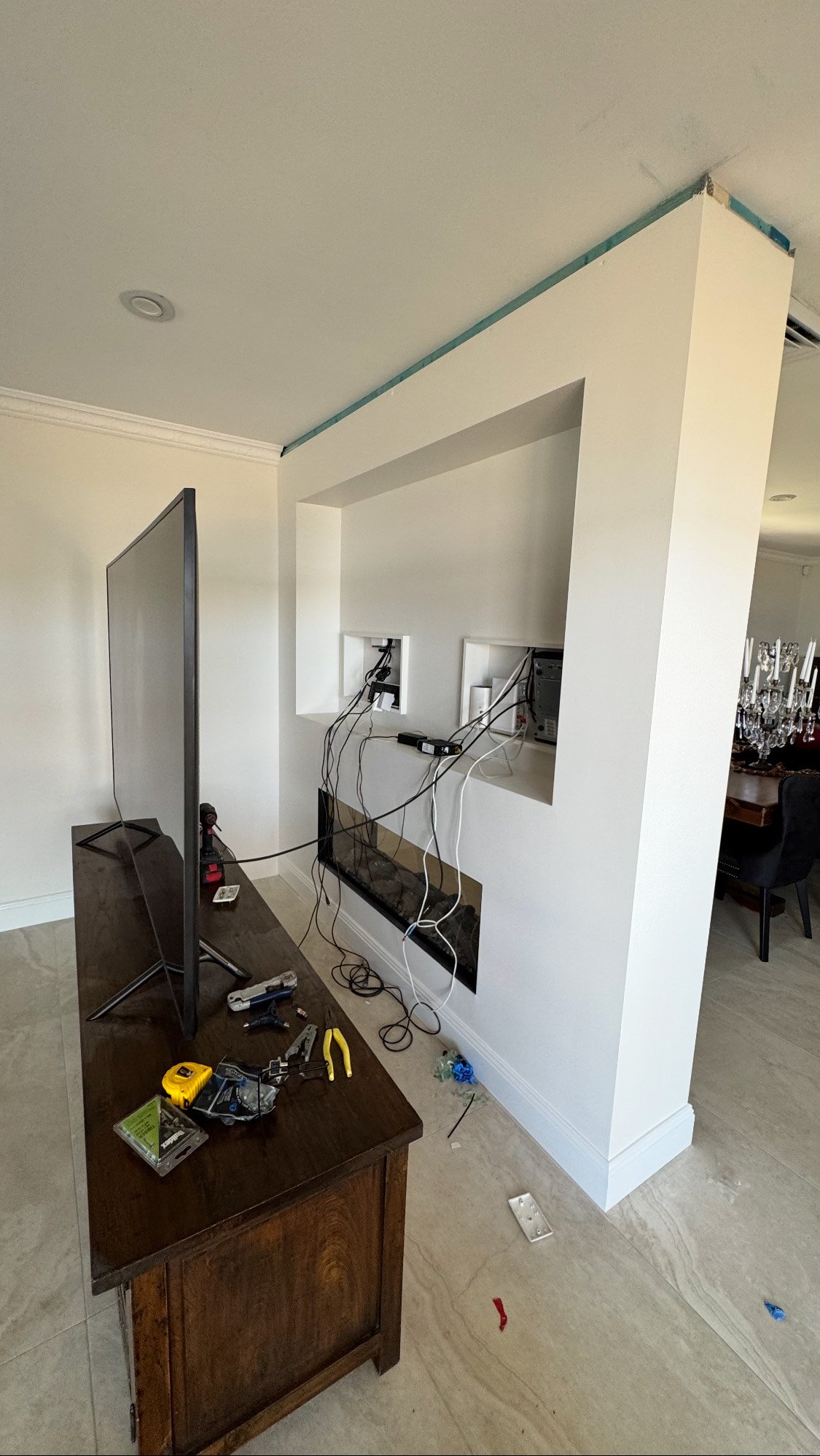 Living room with an unfinished wall with cable connections, a flat-screen TV on a wooden stand, and tools on the table.