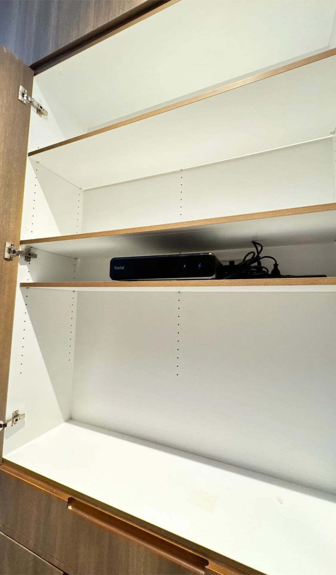 Empty white kitchen cabinet with one device and power cords on the middle shelf.