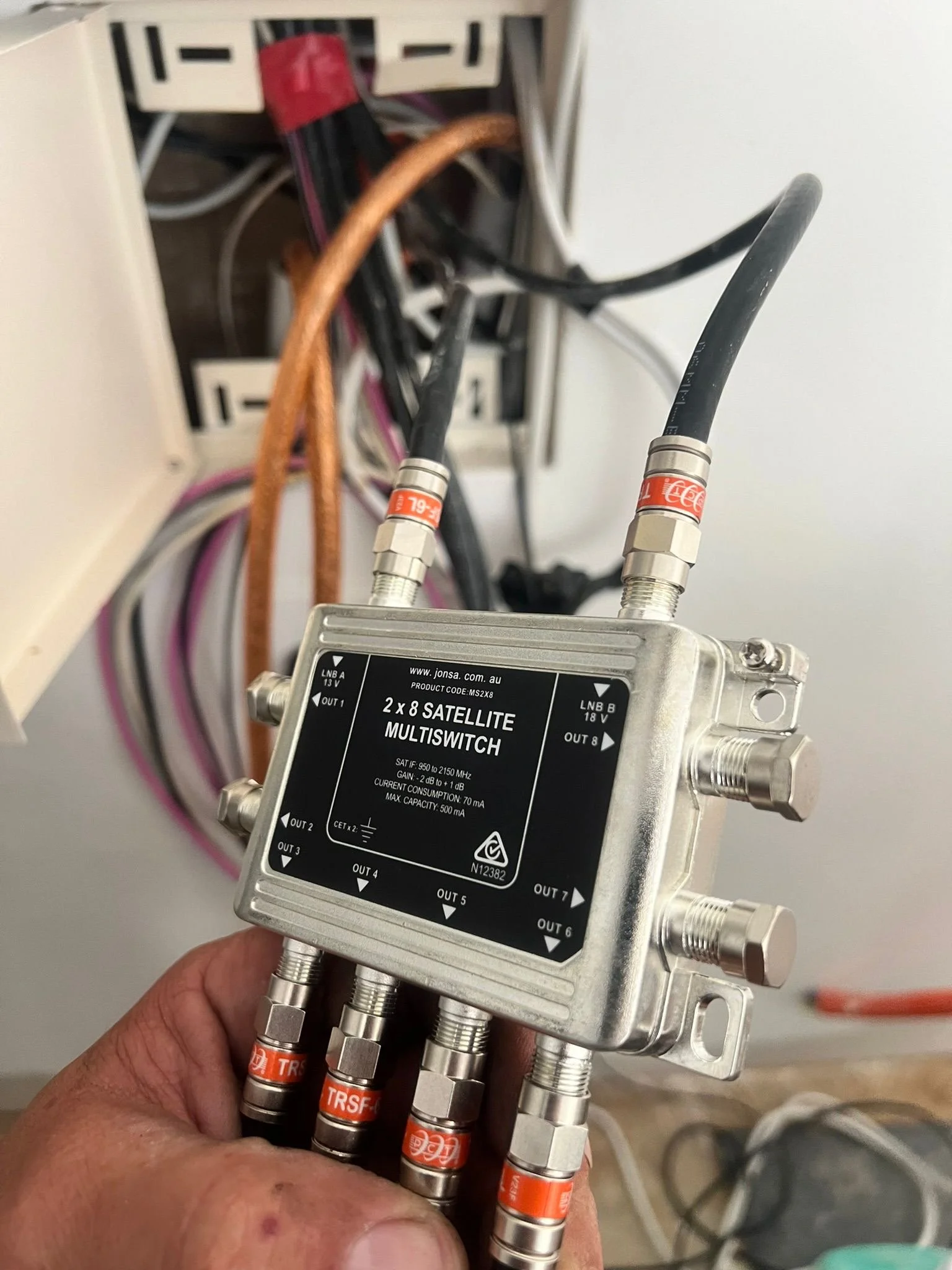 Close-up of a satellite mult-switch with Ethernet cables connected to it, mounted in an electrical box, with multiple colored and black cables in the background.