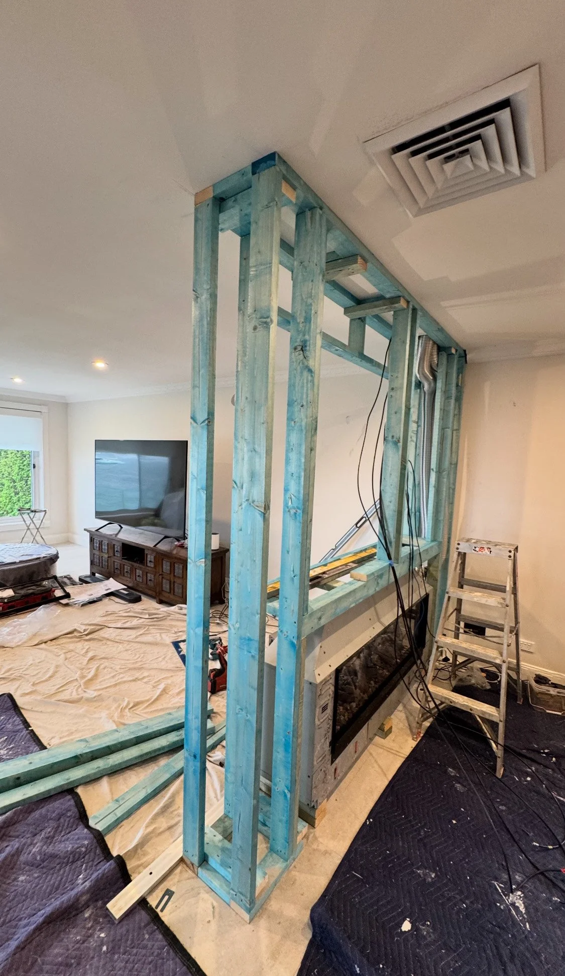 Room undergoing renovation with wooden framing for a wall or structure, ladder nearby, and construction tools around.