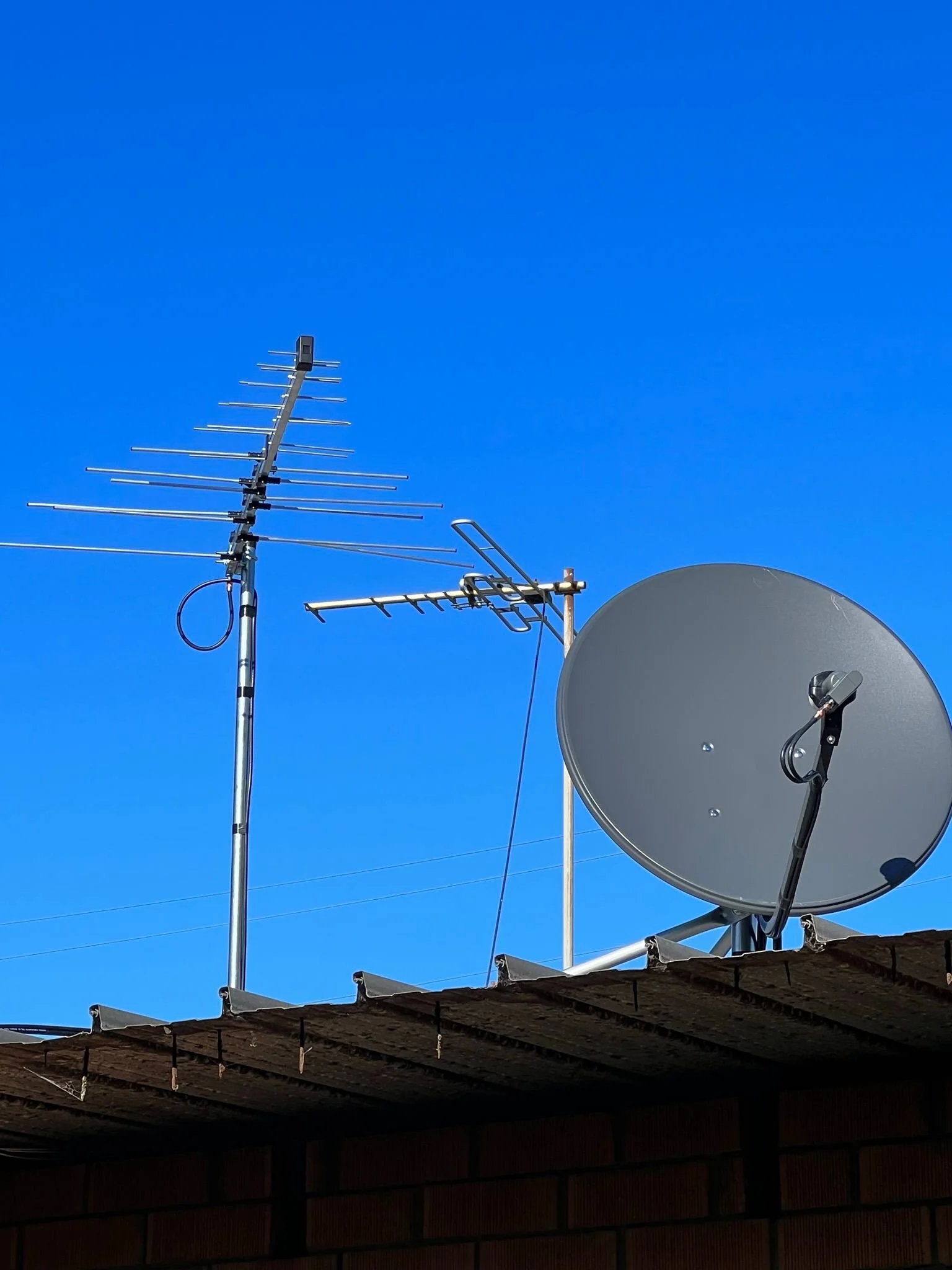 Television antenna and satellite dish on a rooftop against a clear blue sky.