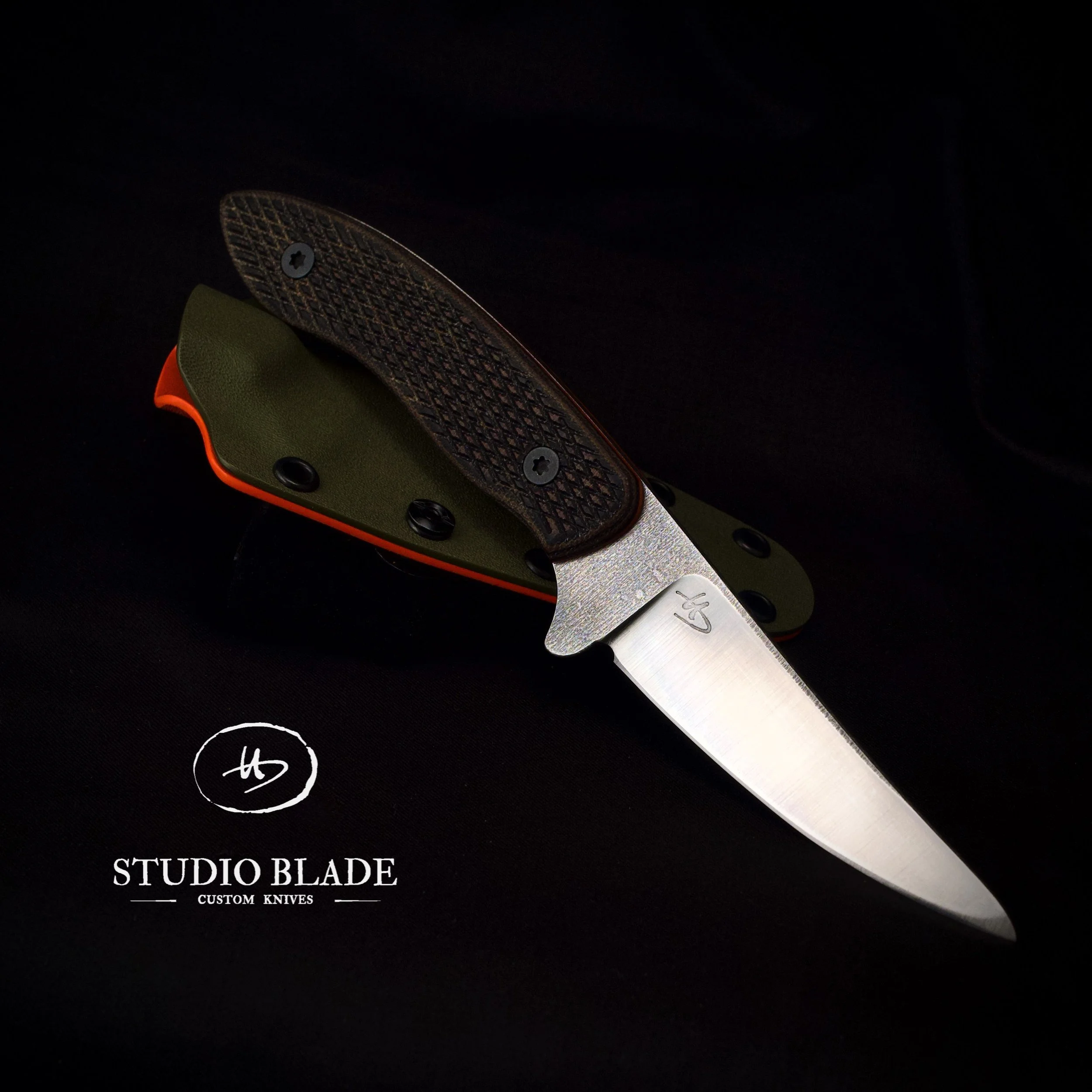 A Studio Blade custom hunting knife with a stainless steel blade and checkered handle, resting on a black surface. The logo 'STUDIO BLADE' is visible in the bottom left corner, along with the words 'CUSTOM KNIVES'.