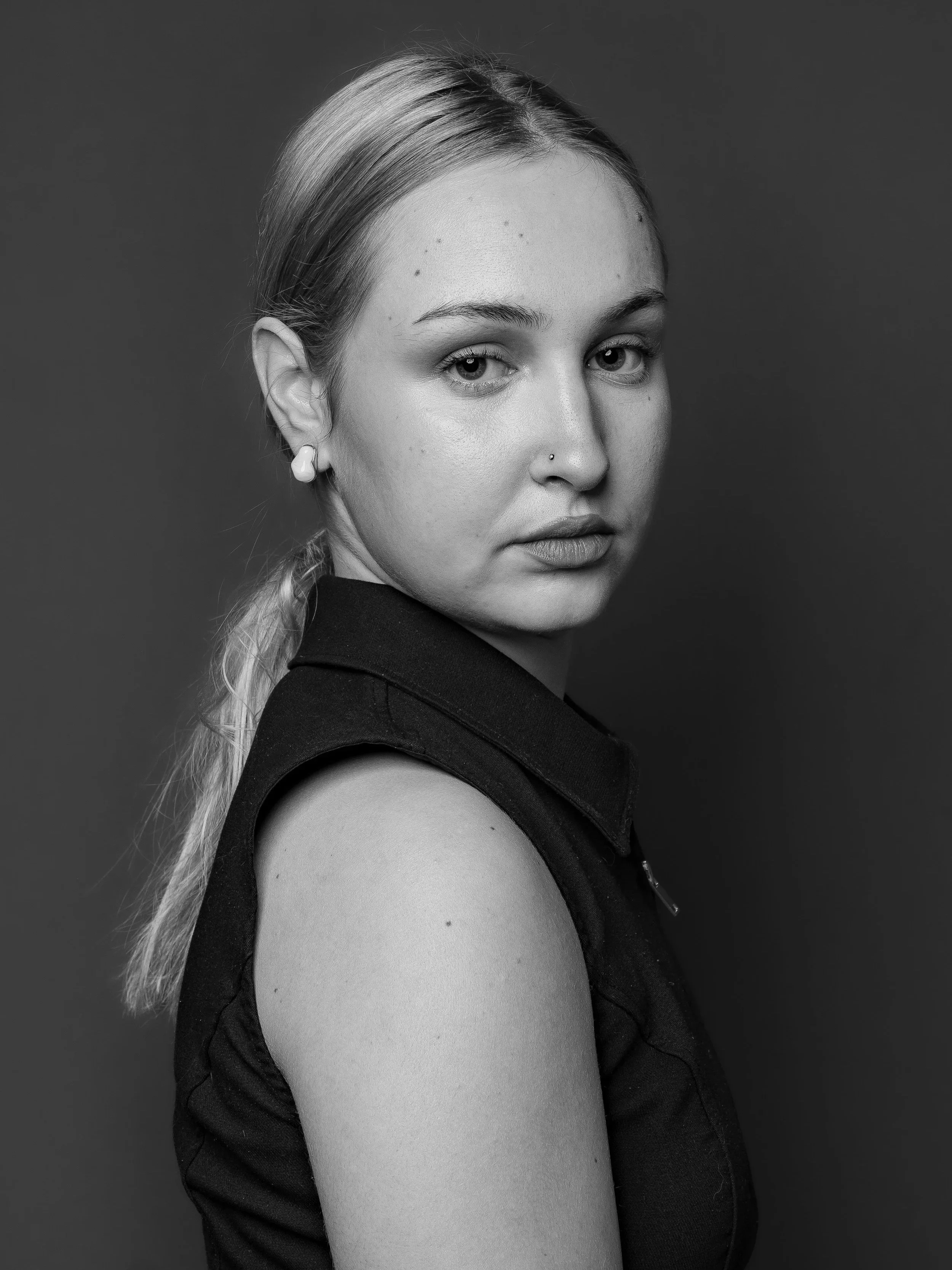 Portrait en noir et blanc d'une jeune femme 'Salomé Biaggi' regardant vers l'appareil, avec une expression neutre, portant un haut sans manches et des boucles d'oreilles.