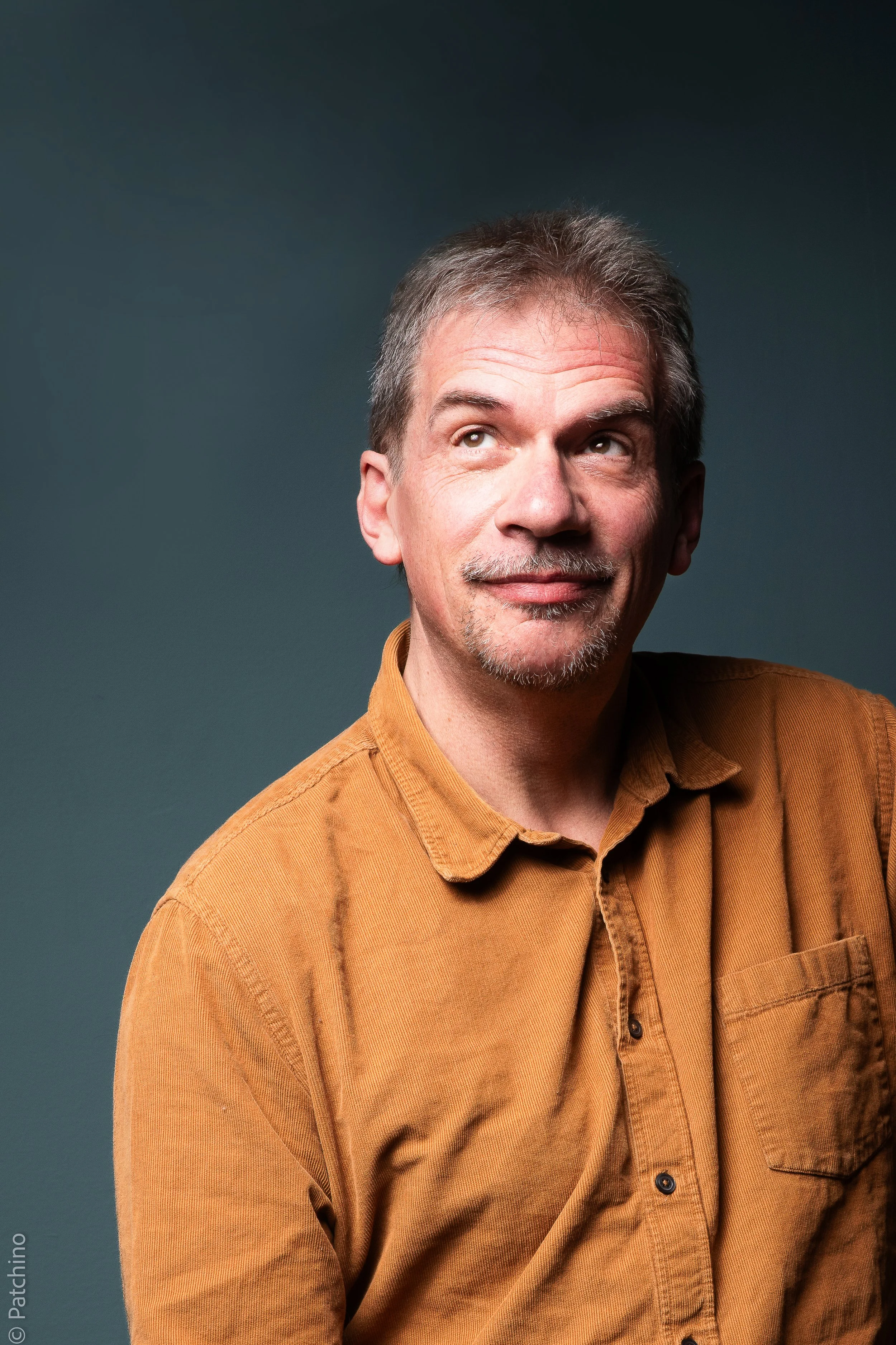 Portrait de Pierre Diot, portant une chemise marron, regardant vers le haut. Fonds gris-bleu.