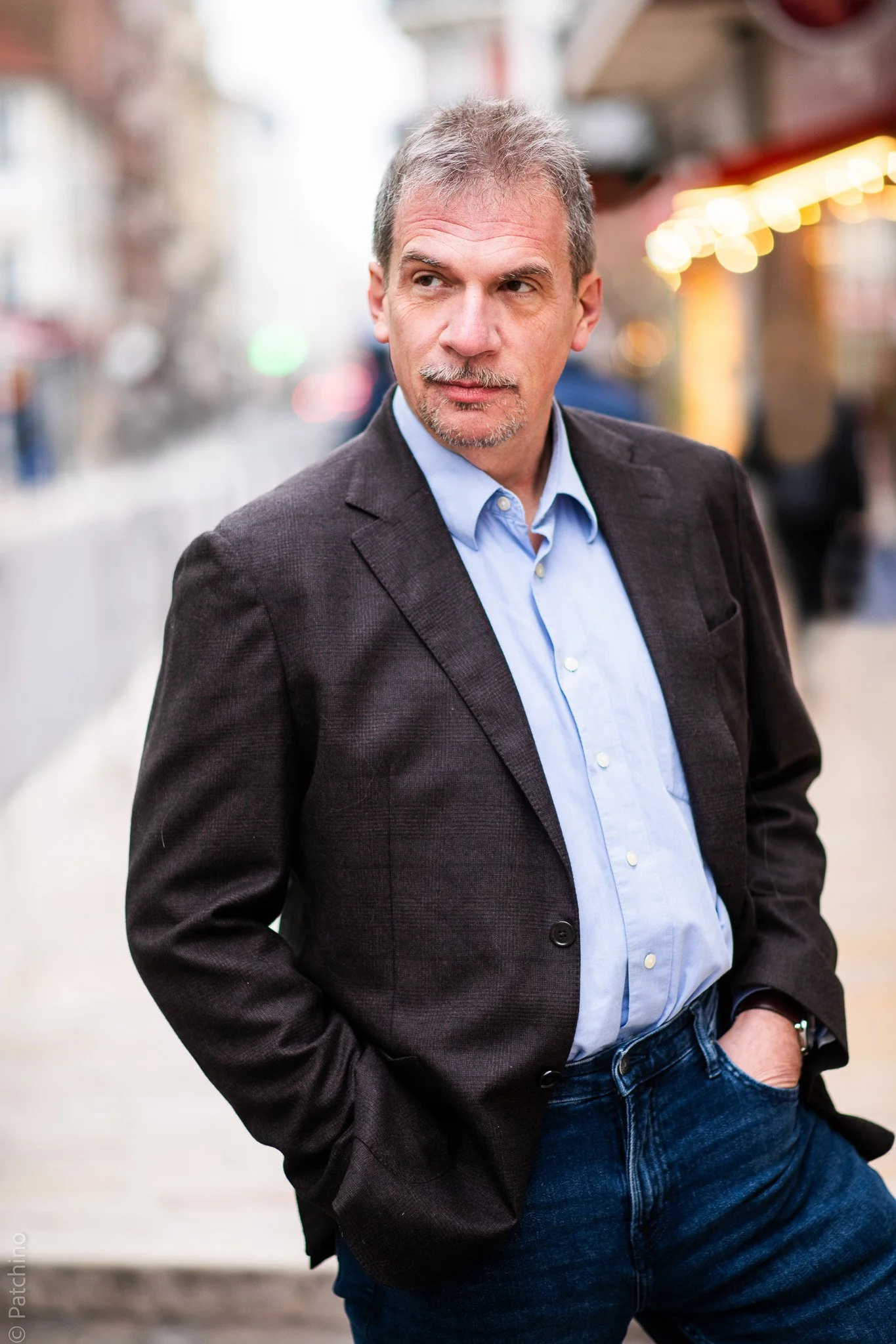 Pierre Diot en blazer noir et chemise bleue, marchant dans une rue urbaine lumineuse