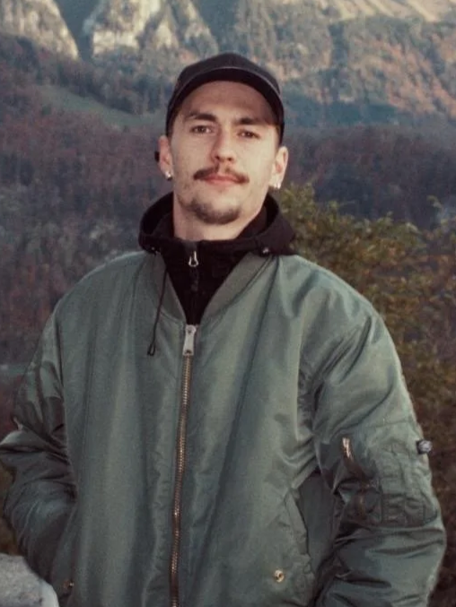 Jeune homme 'Théo Martin' avec une casquette et une veste en extérieur avec un paysage de montagnes en arrière-plan.