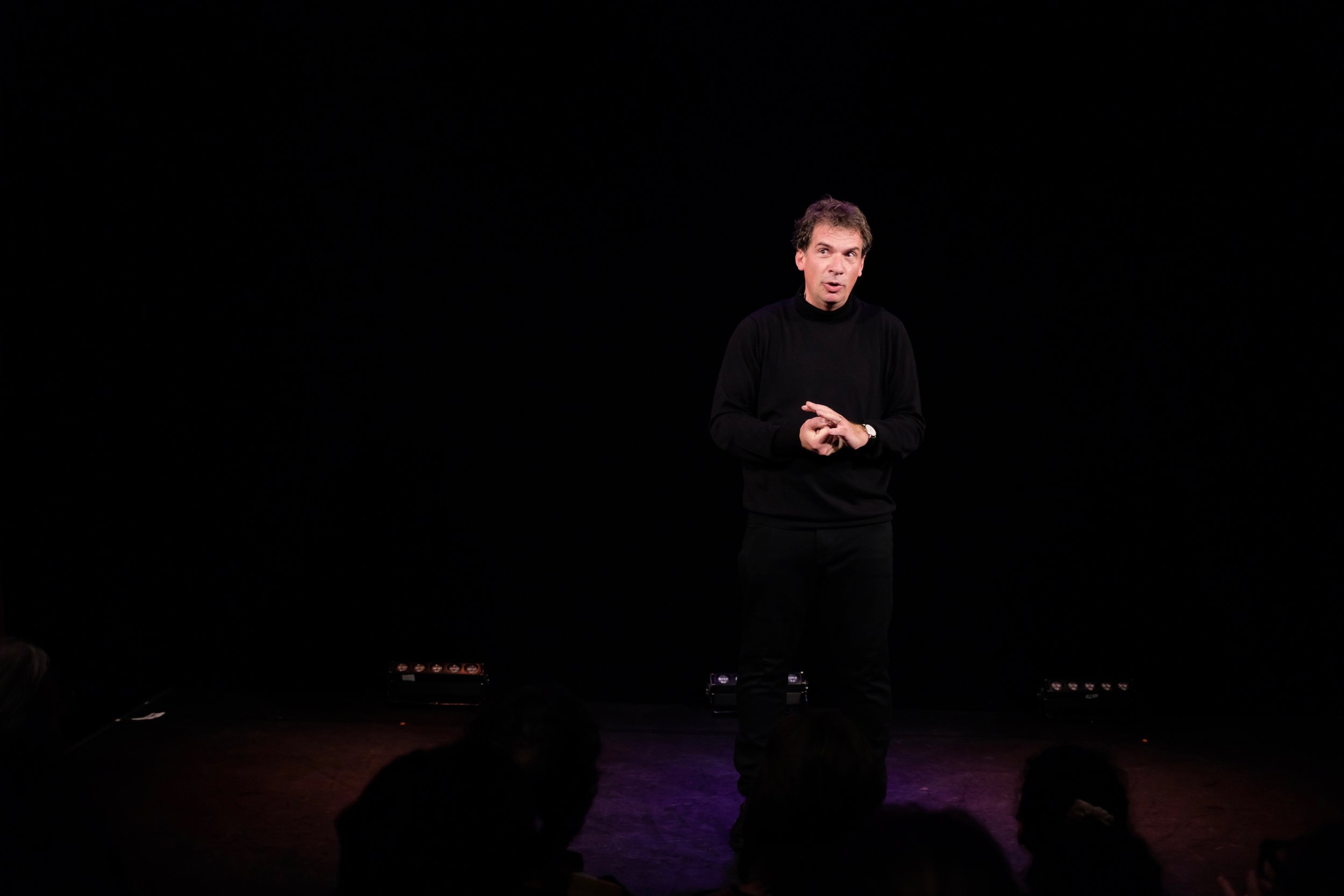 Pierre Diot devant un public dans une scène sombre.