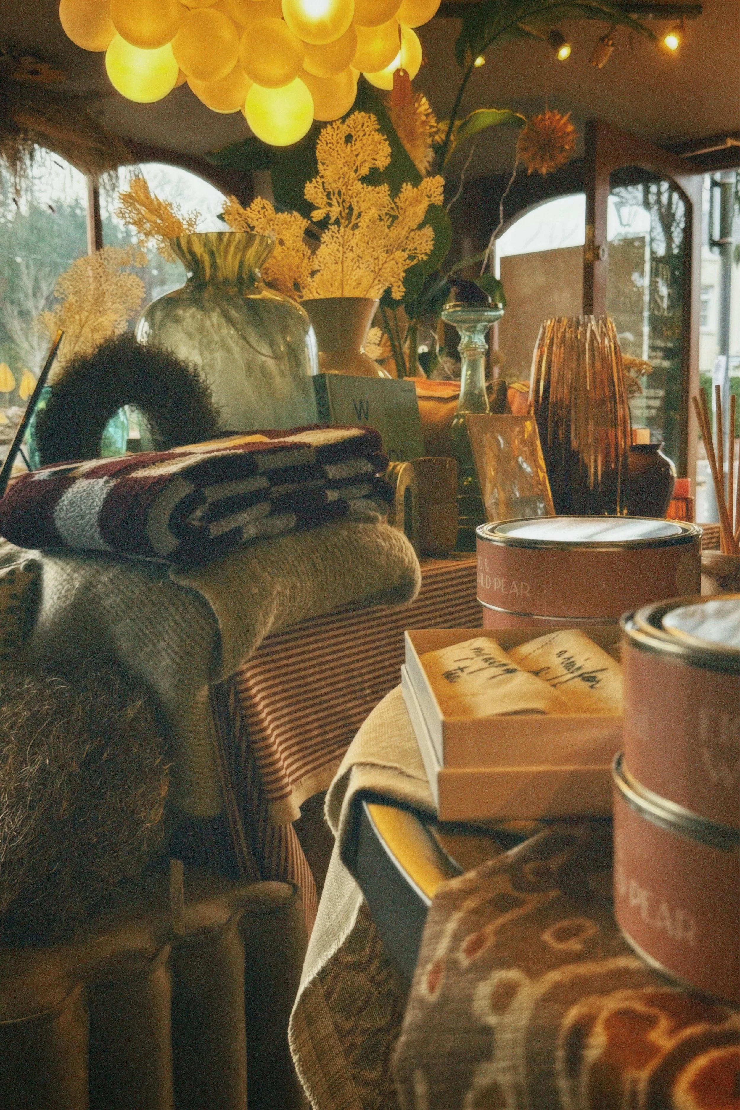 Interior of a cozy cafe or shop decorated with vases, flowers, and decorative items, with striped and cloth table coverings and various containers.