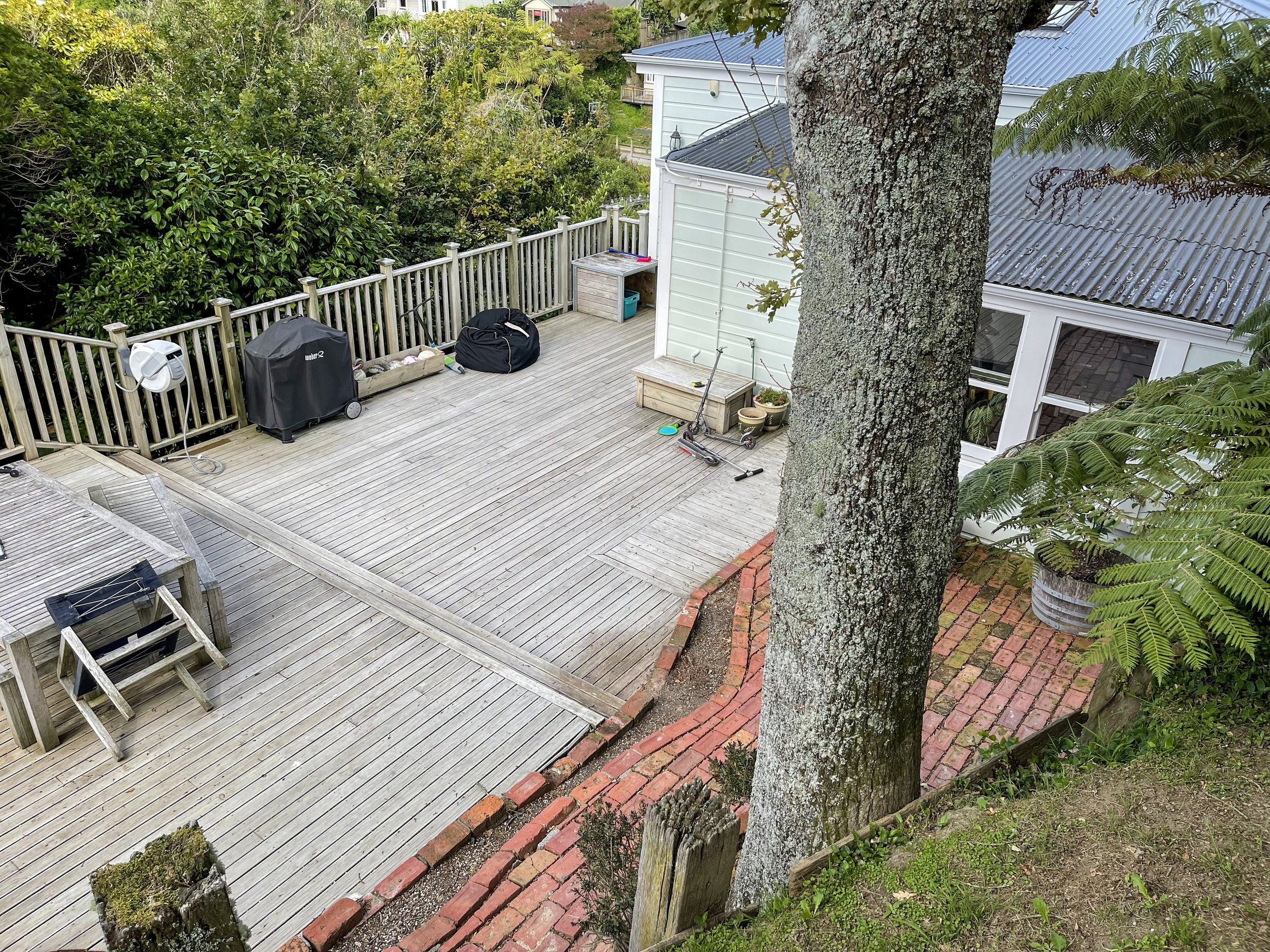 An overview of the site, boasting a large tree, random brick work, and aged decking.