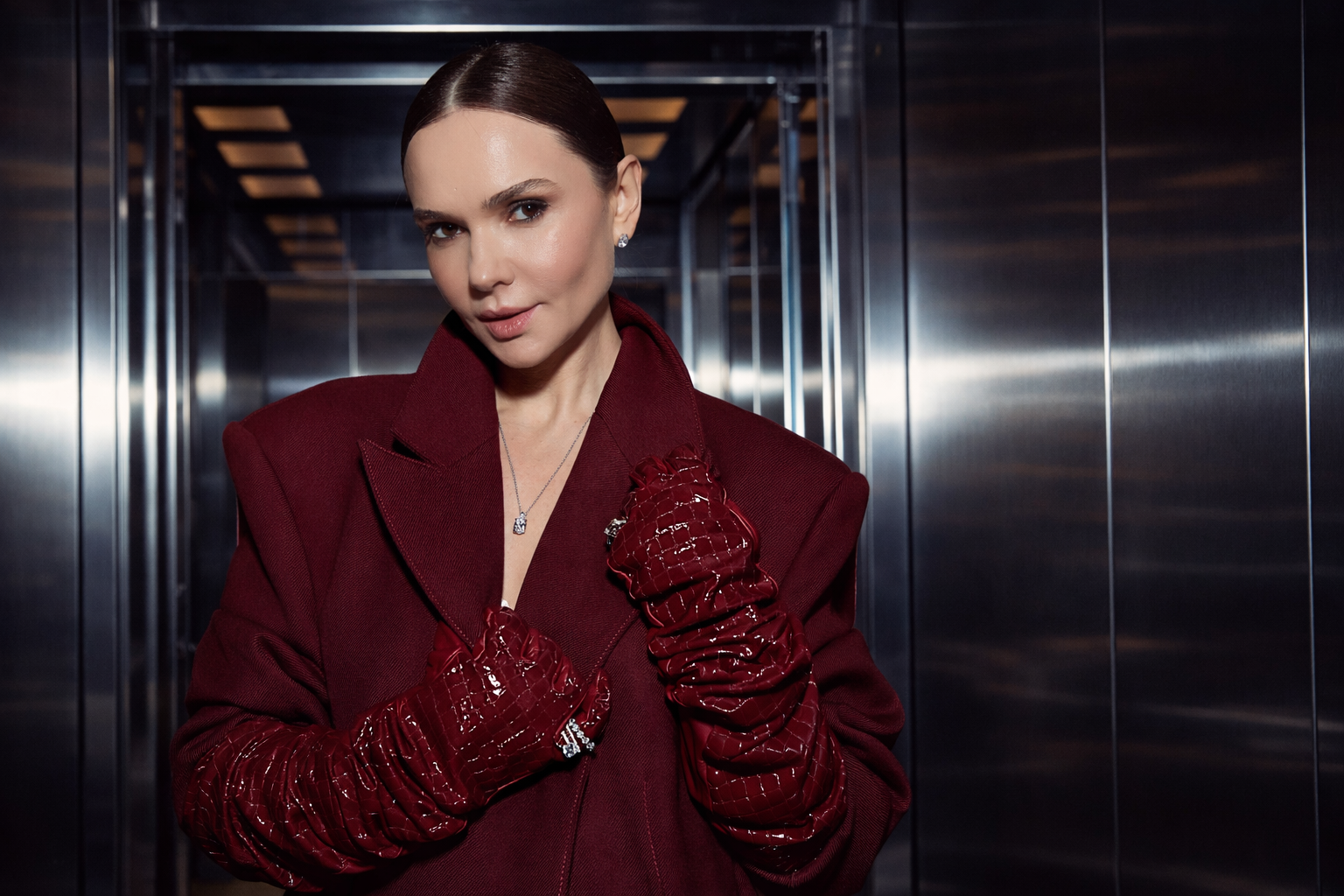 Woman in a red blazer and matching red gloves standing in an elevator.