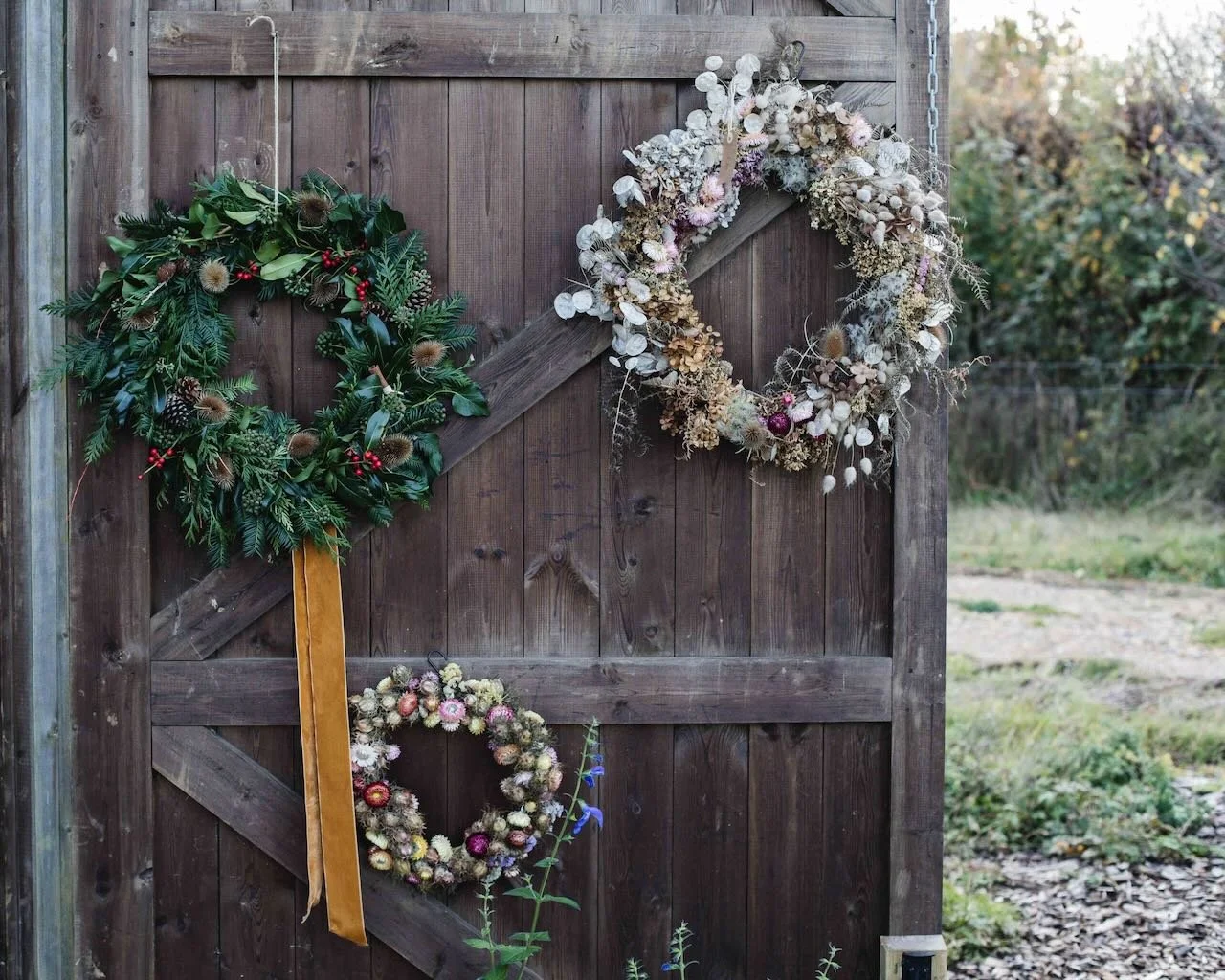 Three decorative wreaths hanging on a wooden gate outdoors during daytime.