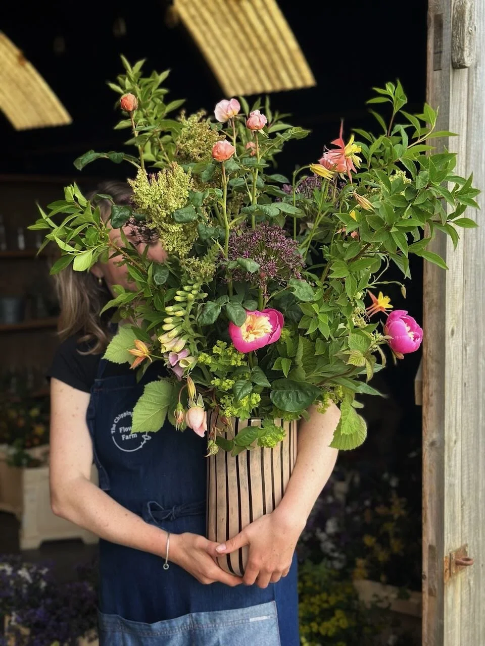 Person holding a large bouquet of colorful flowers and green foliage in a striped wooden container.