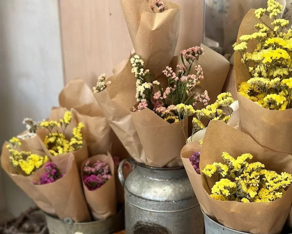 Assorted small bouquets of colorful flowers wrapped in brown craft paper, arranged in vintage metal containers.