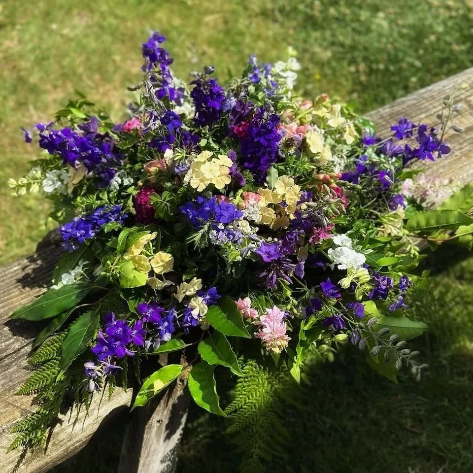 Brightly colored mixed flowers arranged on a weathered wooden plank outdoors.