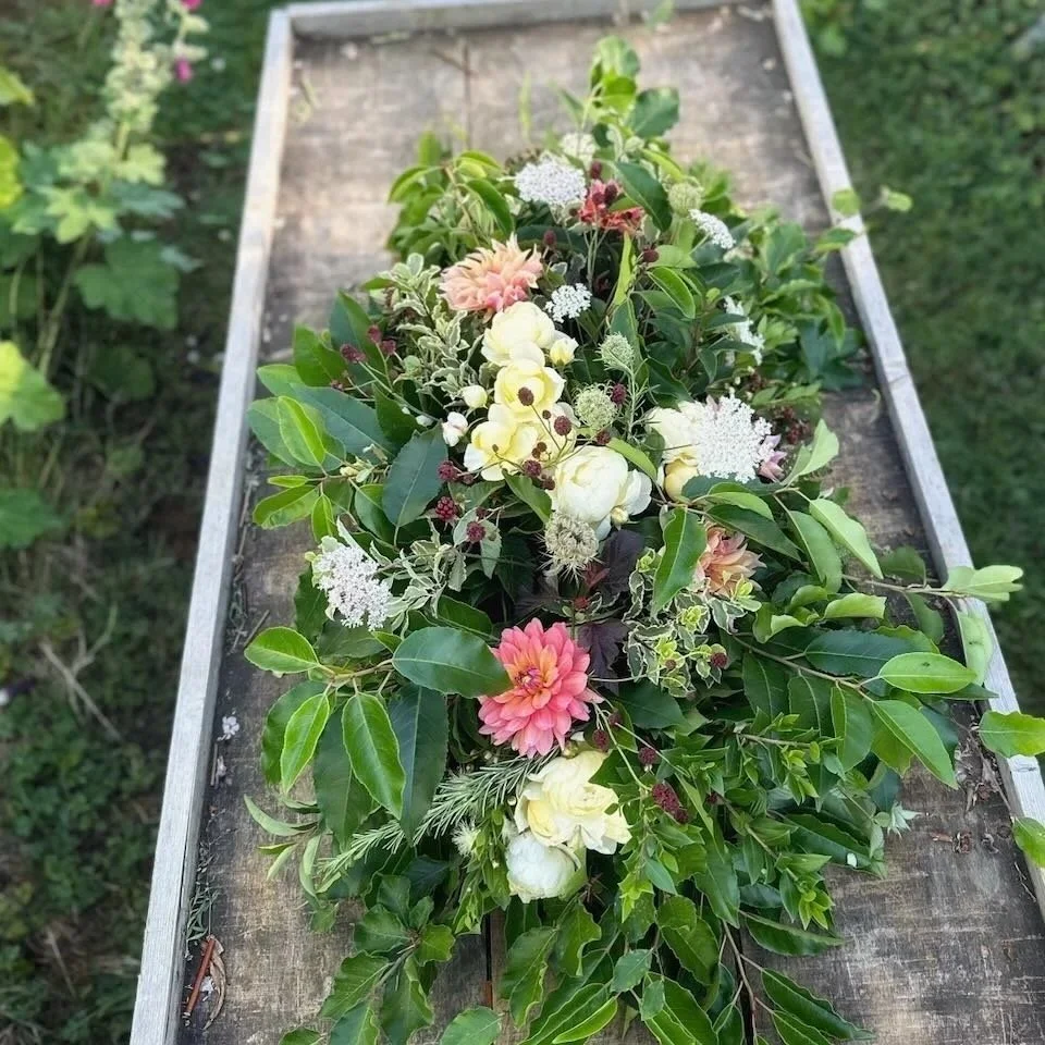 Freshly gathered bouquet of various flowers and green leaves on a wooden table outdoors.