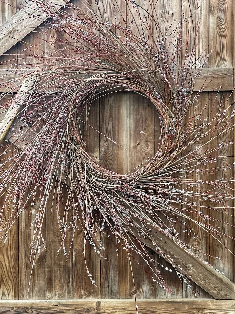 A decorative circular arrangement made of thin branches with small white buds, mounted on a wooden fence.