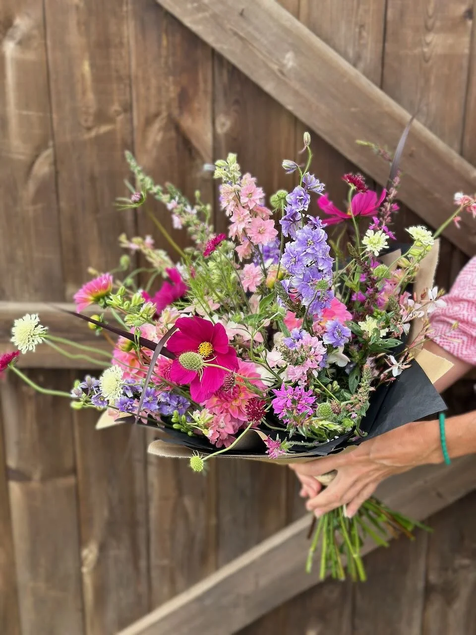 Person holding a colorful bouquet of flowers in front of a wooden fence.