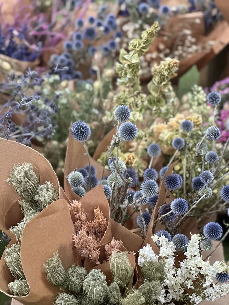 Bouquets of dried flowers with various textures and colors, wrapped in brown paper.