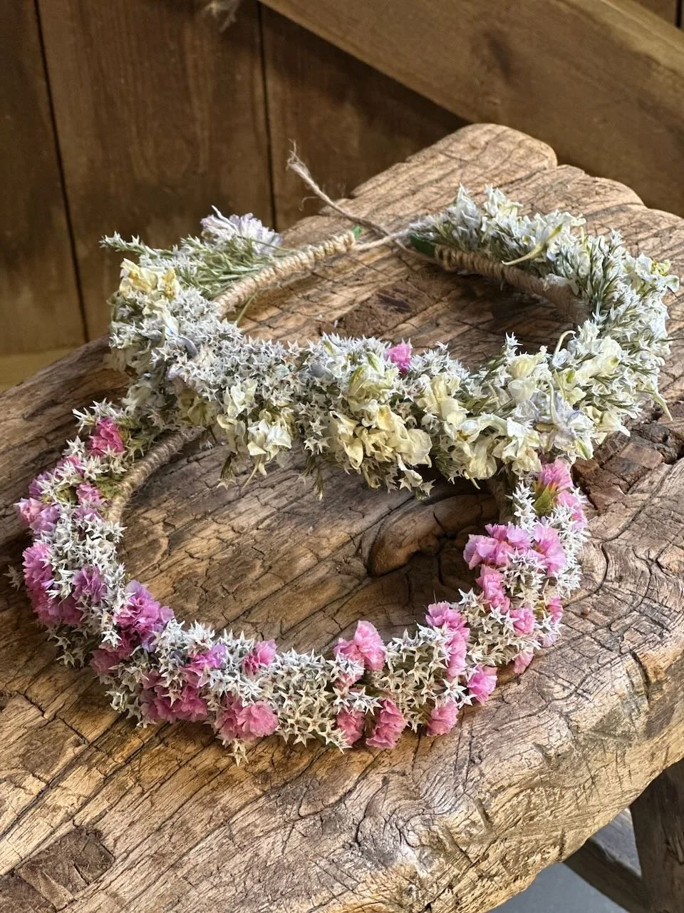 Two floral wreaths made of small pink, white, and lavender flowers rest on a rustic wooden surface.