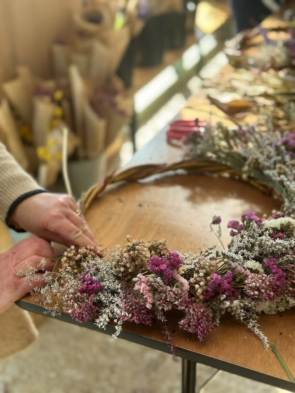 Person arranging dried flowers into a wreath on a wooden table in a flower shop.
