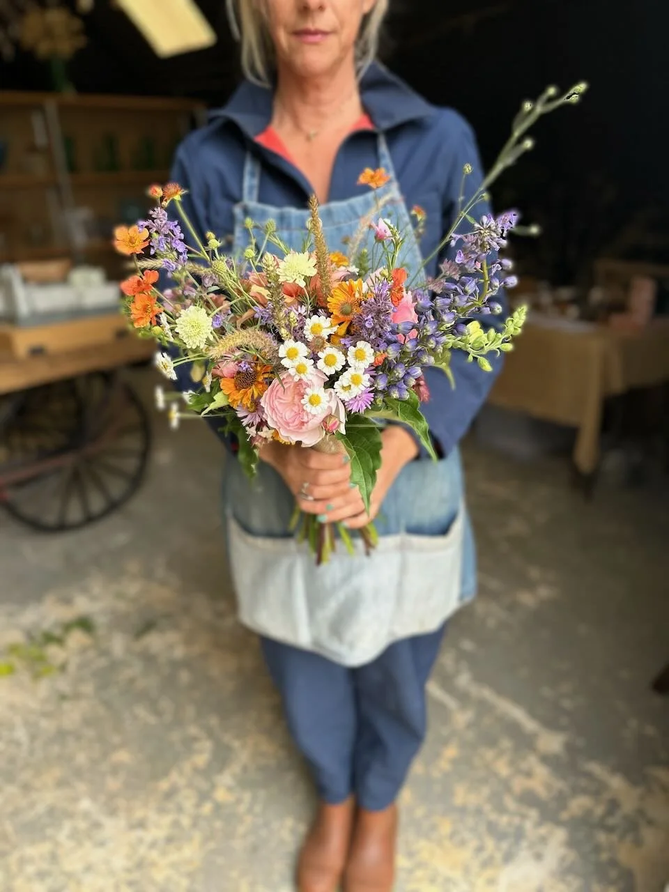 Woman holding a colorful bouquet of wildflowers in a rustic setting.