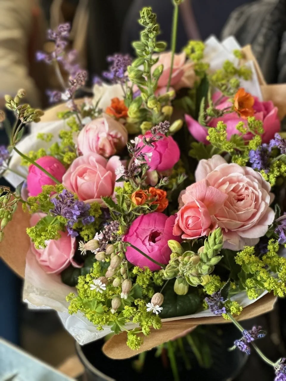 A bouquet of various pink, purple, orange, and cream flowers with green foliage.