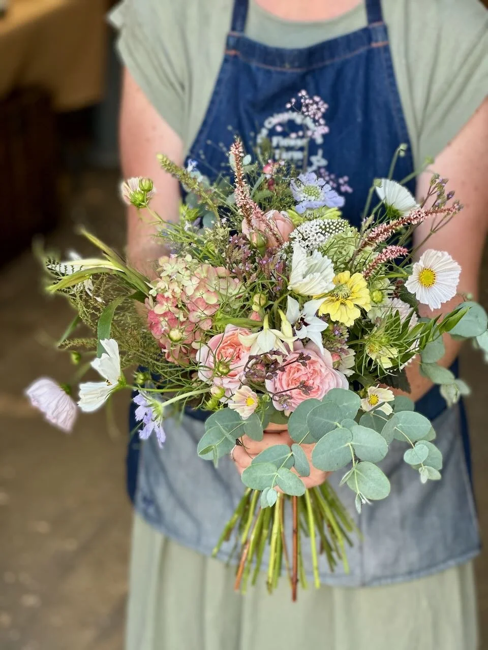Person holding a bouquet of mixed flowers including pink roses, white daisies, and green eucalyptus leaves.