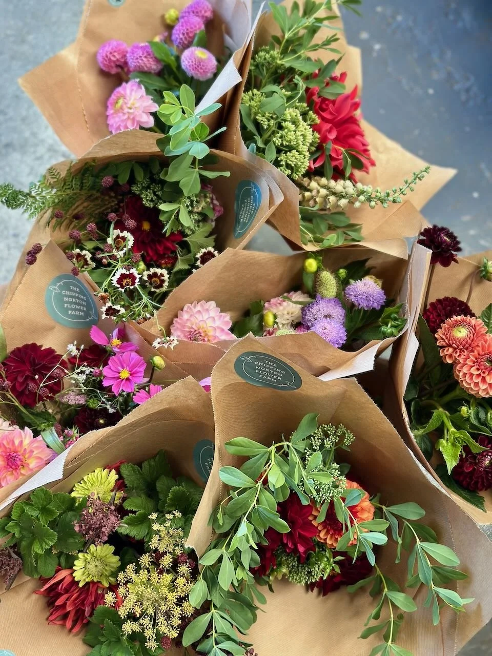 Multiple bouquets of fresh flowers wrapped in brown paper on a concrete surface.