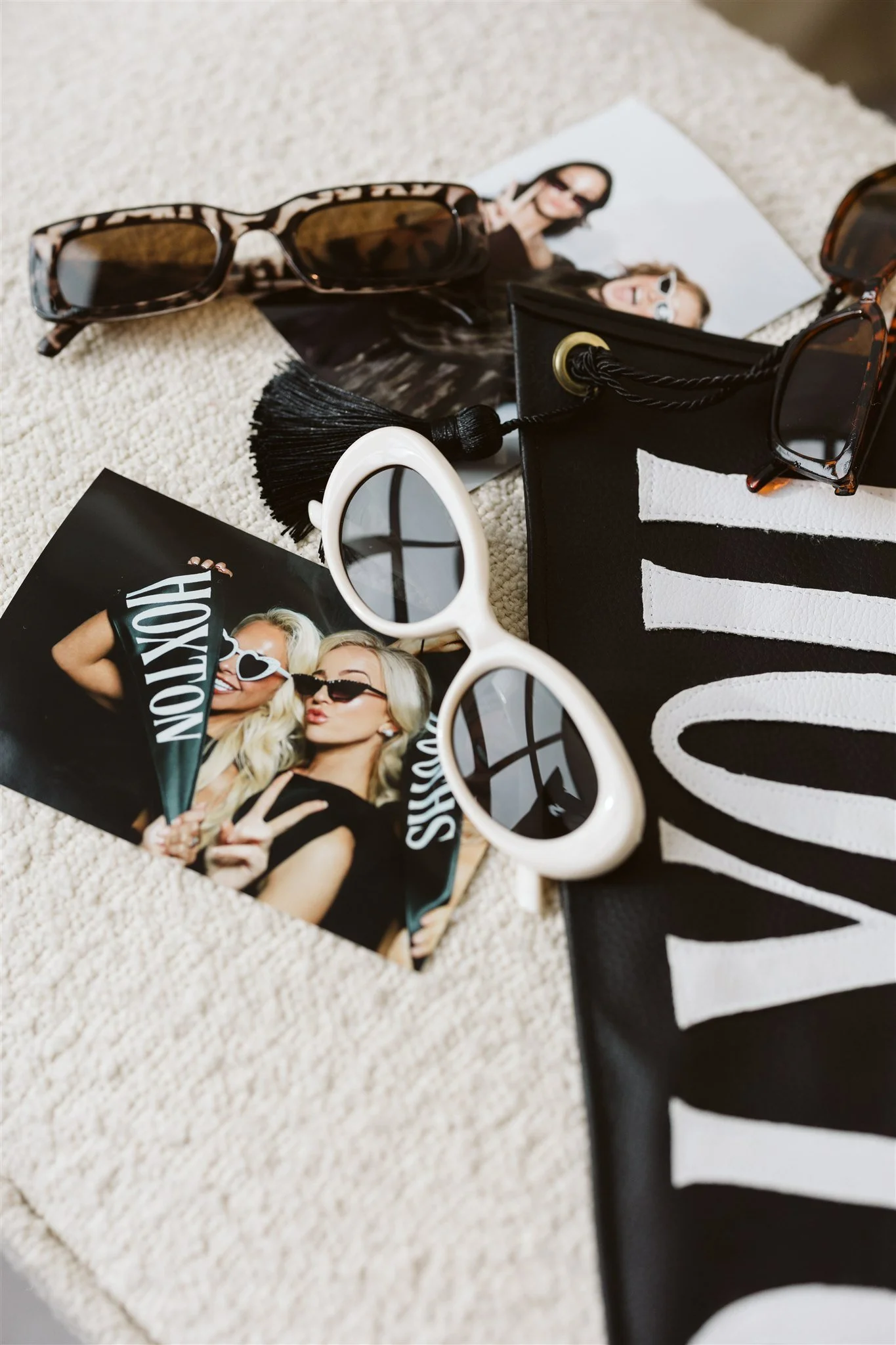 Fashion accessories including sunglasses, photos of women, and cosmetic items arranged on a textured surface.