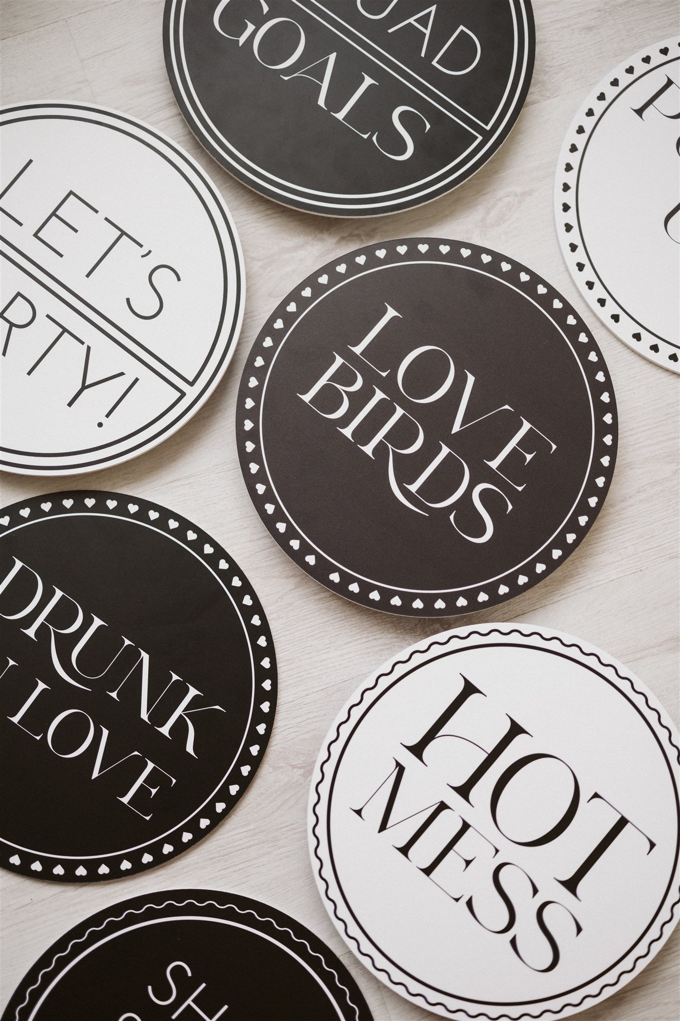 Collection of round black and white signs with humorous messages such as "Love Lists," "Hot Mess," "Drunk in Love," and "Go To Goals."