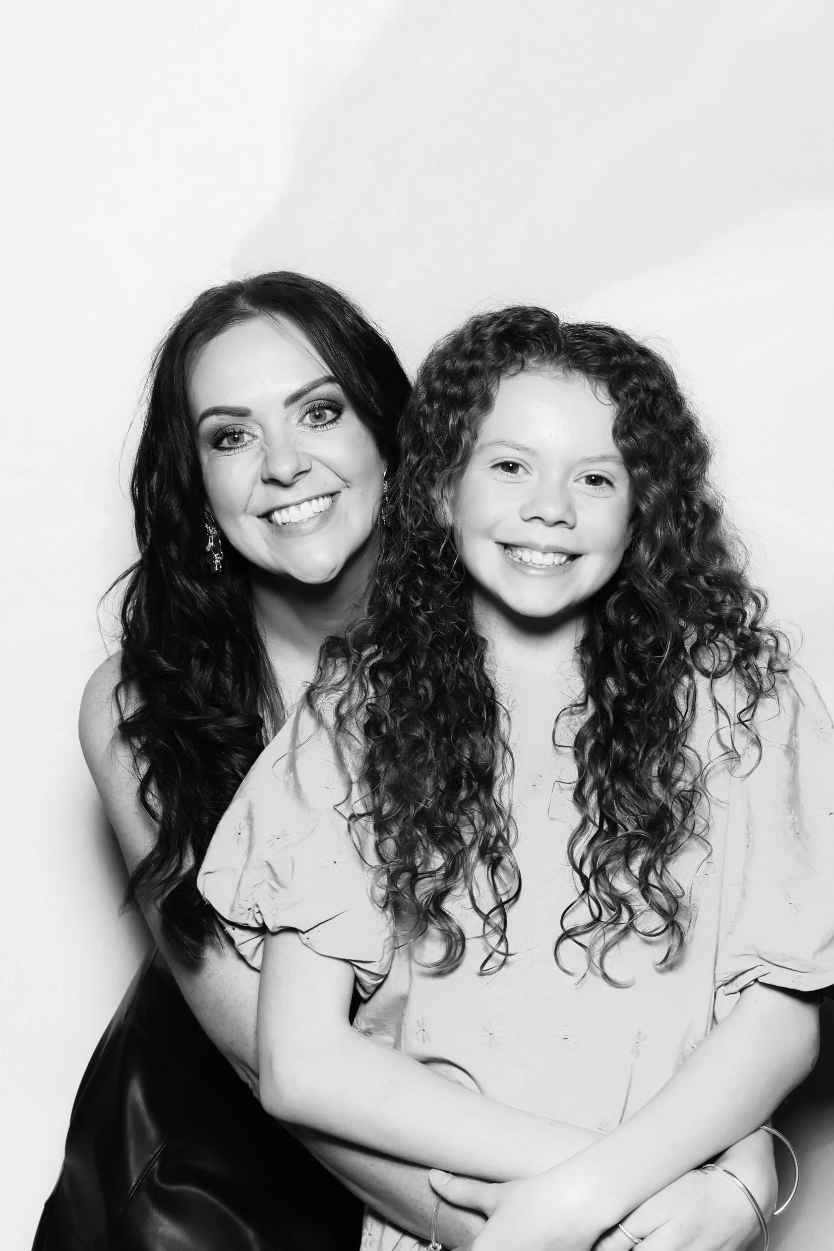 Black and white photo of a smiling woman with long dark hair and a young girl with long curly hair, both looking at the camera.