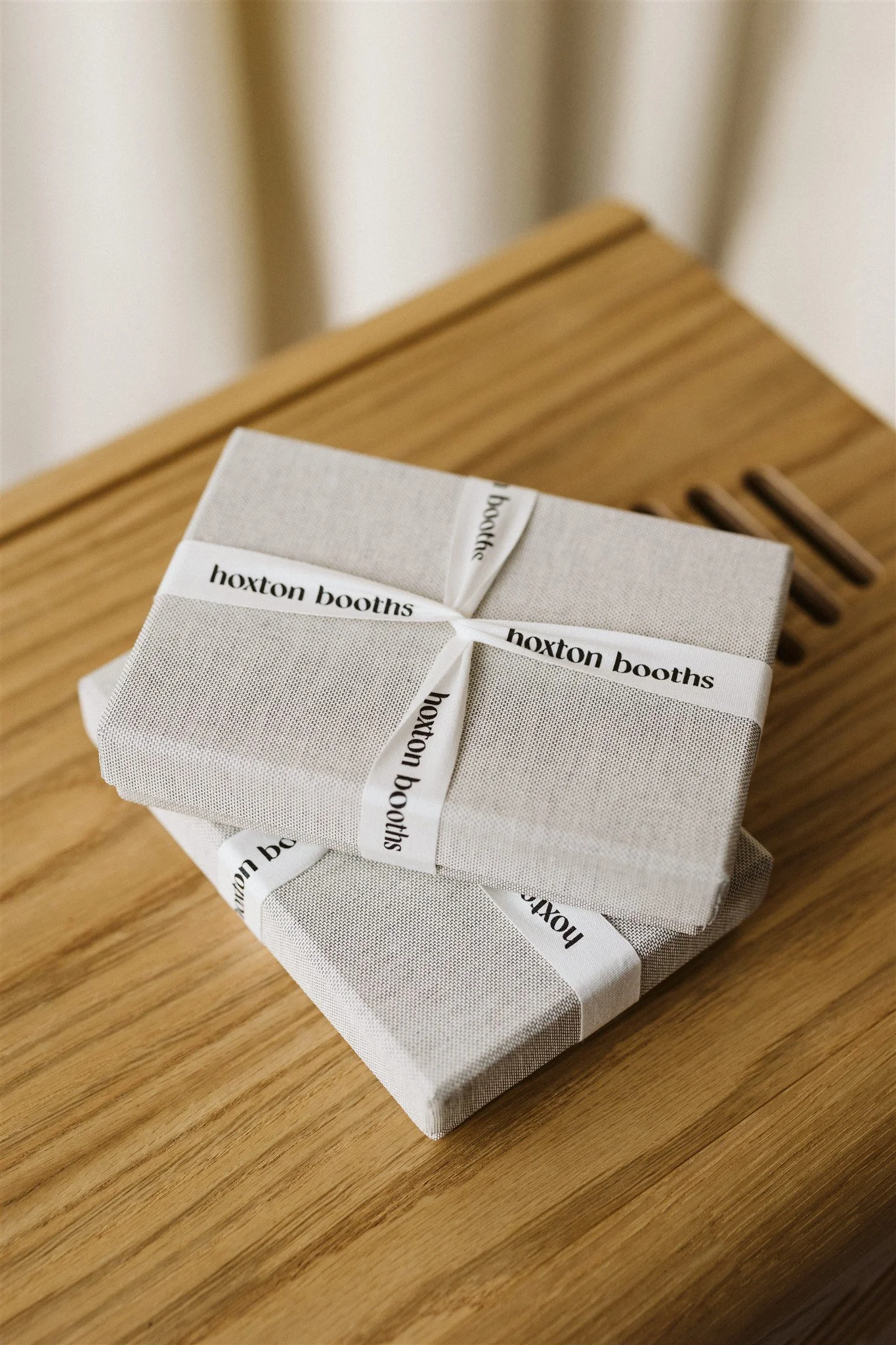 Two neatly wrapped gift boxes on a wooden surface, each with white ribbon labeled 'hoxton booths'.