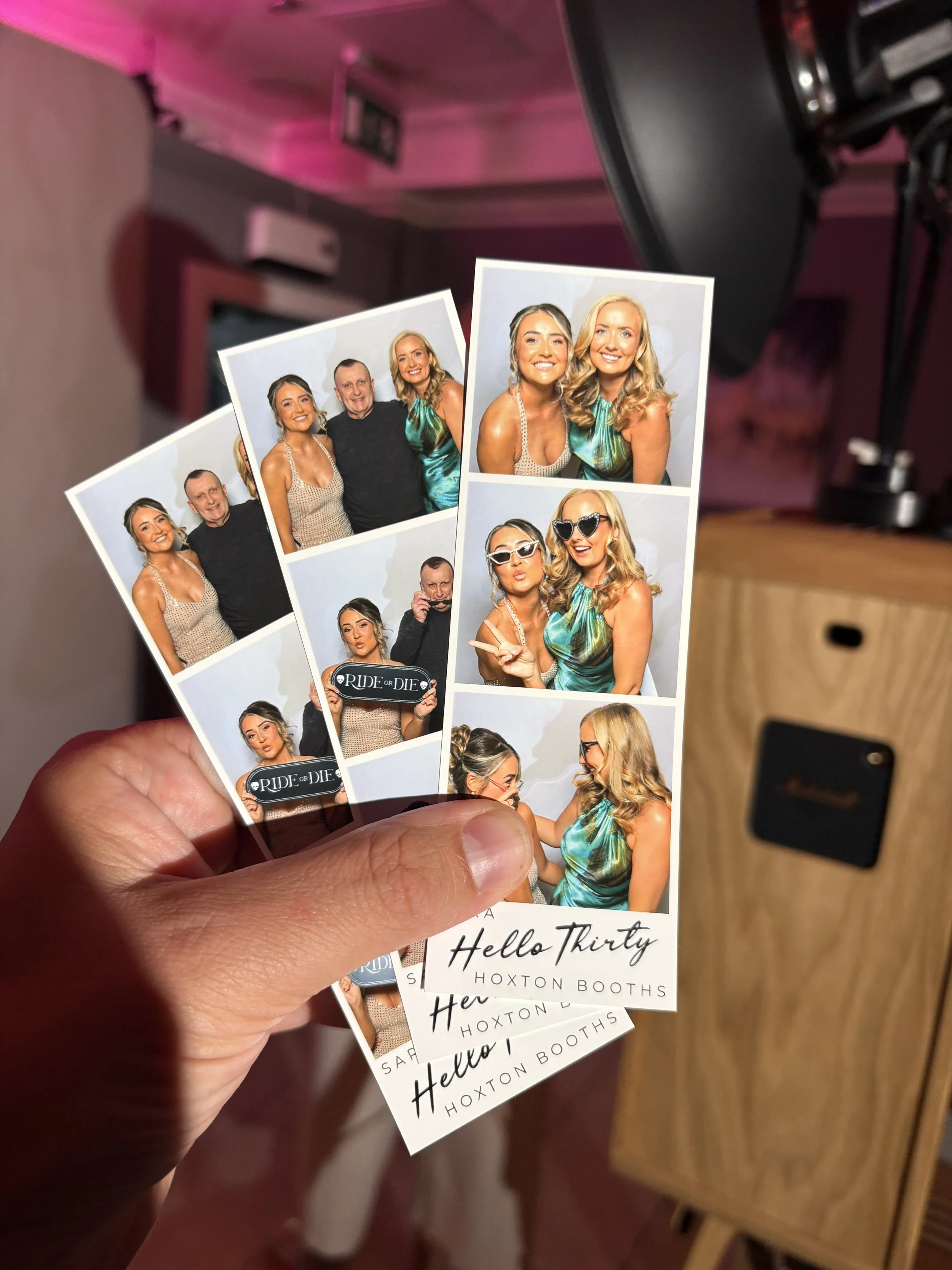 Two photo booth strips featuring four women and one man in some photos and alone in others, with a wooden cabinet and a black speaker in the background.