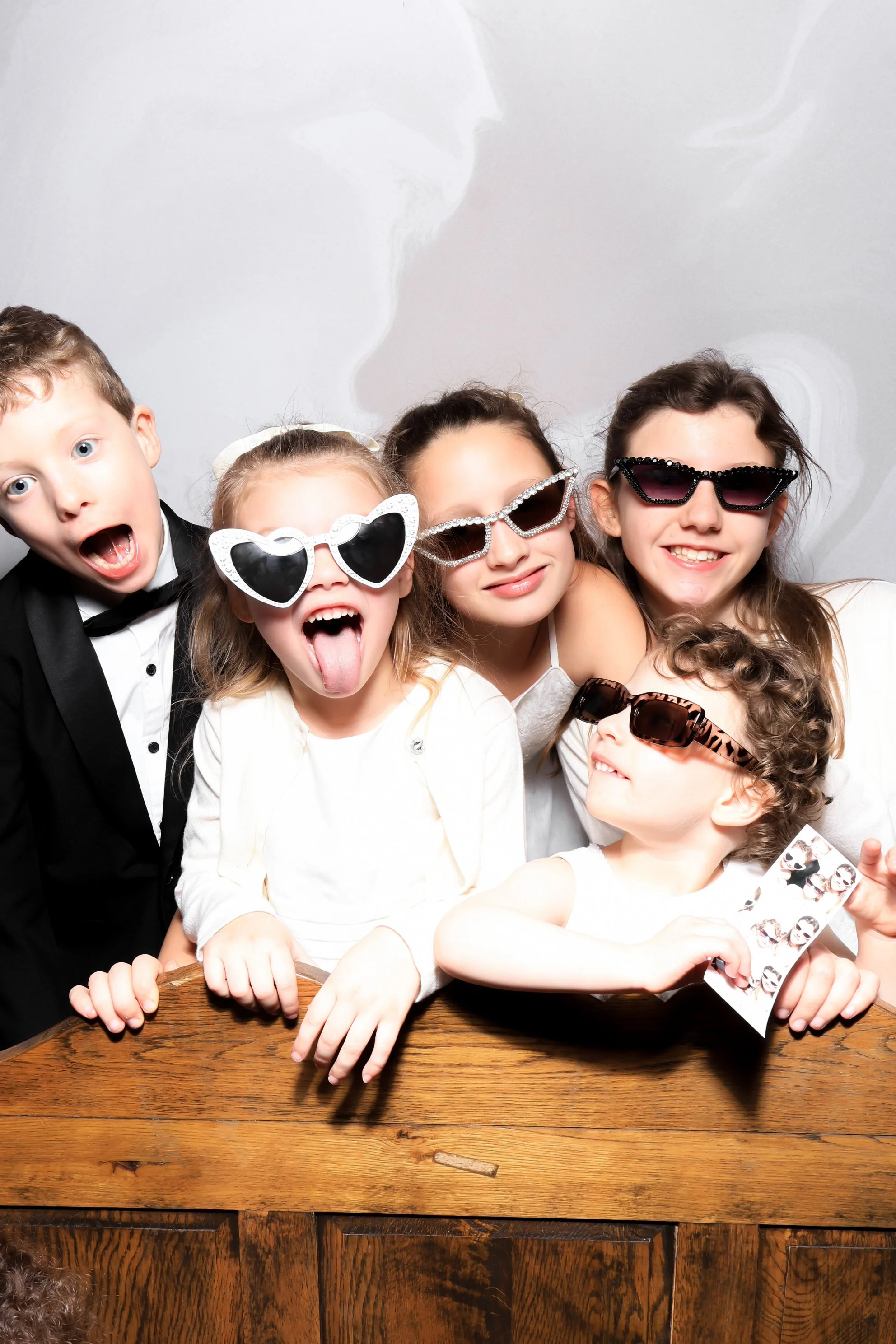 Group of children wearing sunglasses and making silly faces at a photo booth.