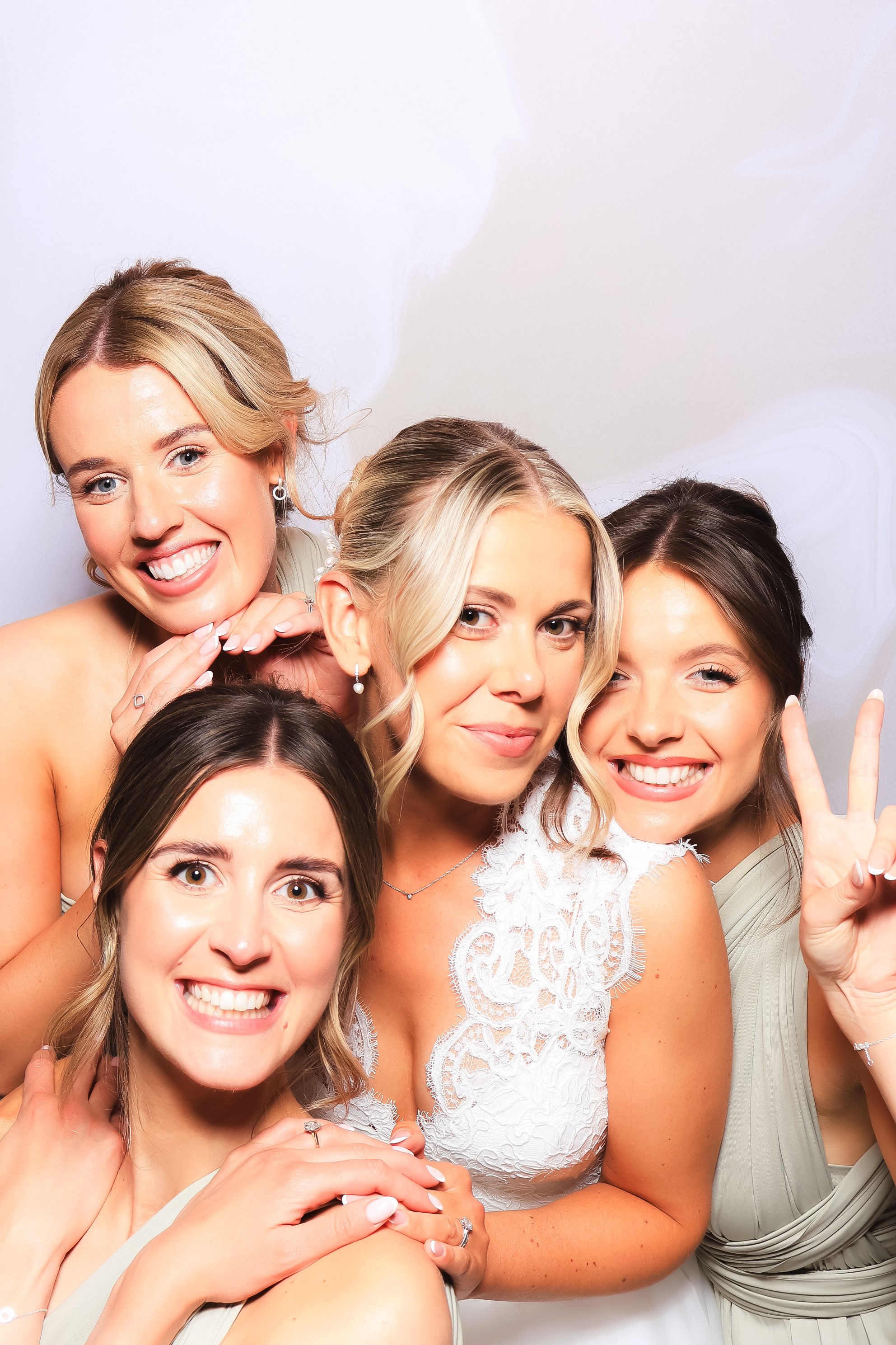 Group of five women smiling and posing together, one making a peace sign, at a celebration or event.