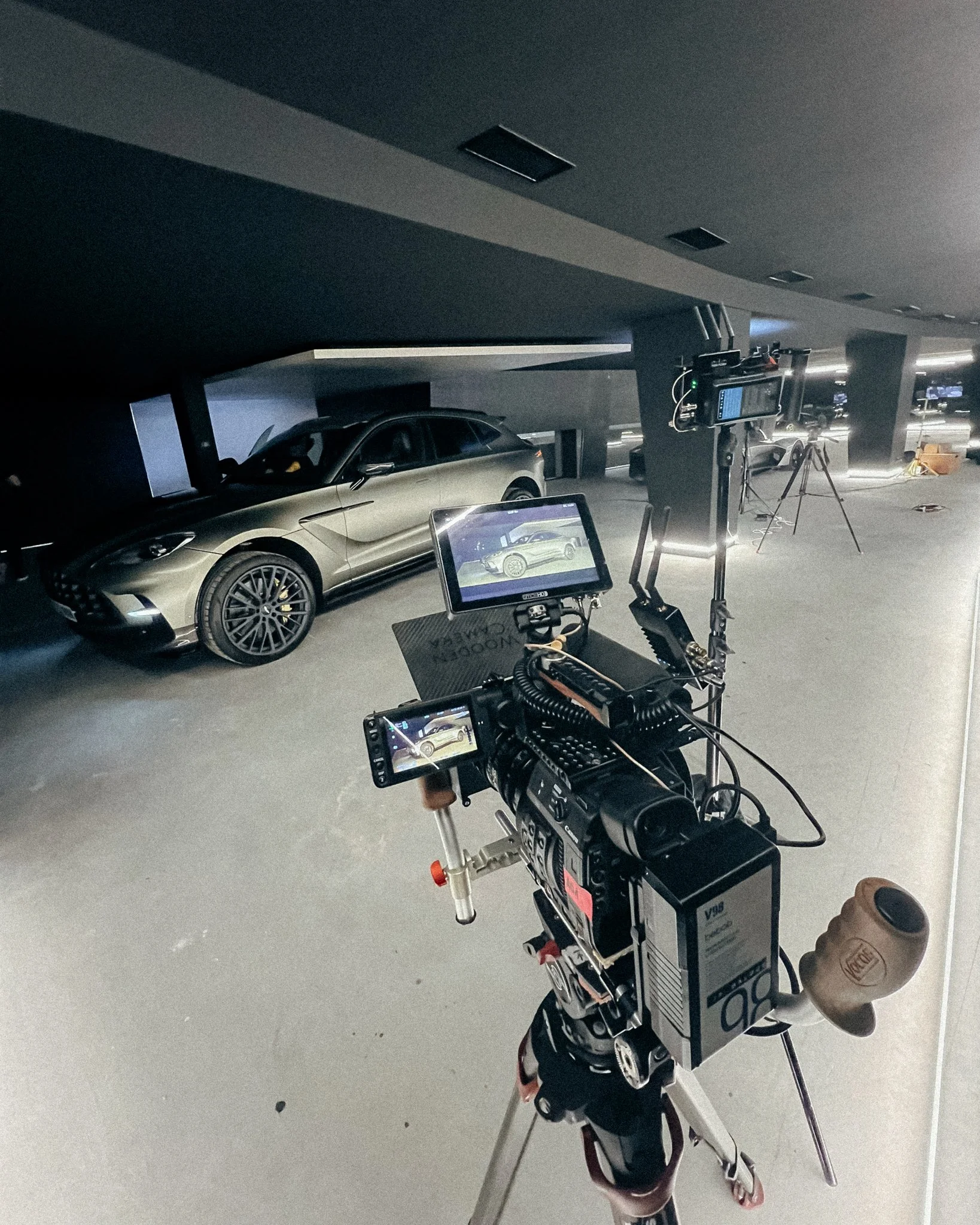A camera on a tripod capturing the image of a gray luxury car inside a parking garage or underground parking lot.
