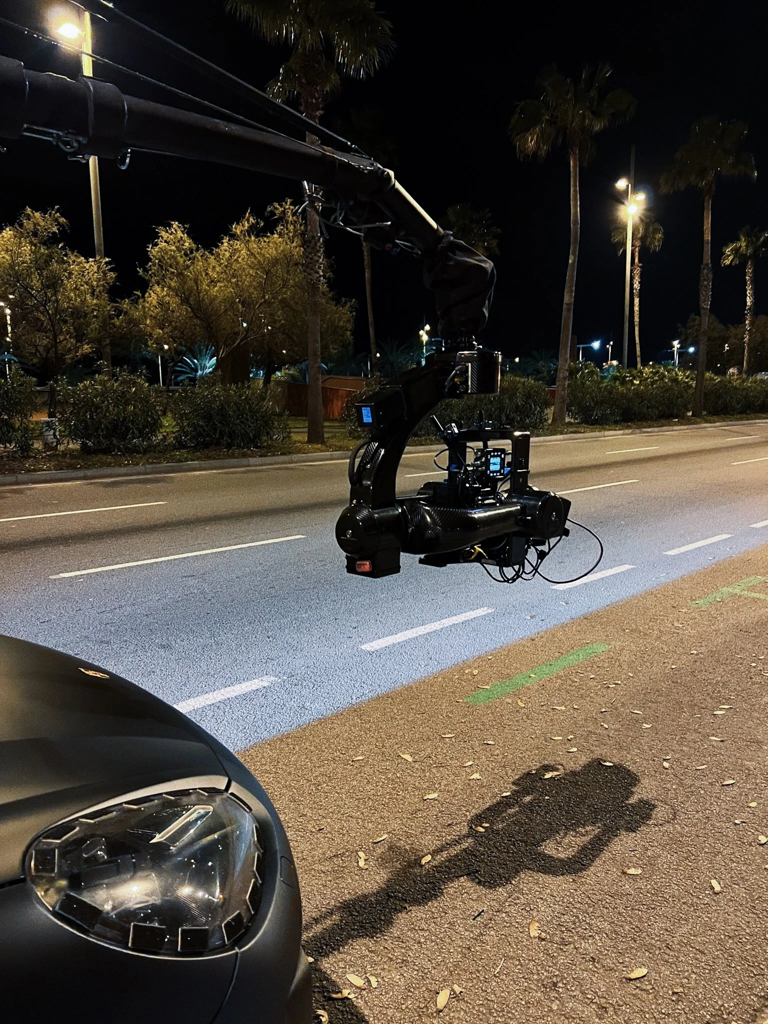 Camera crane on a city street at night with palm trees and streetlights in the background.