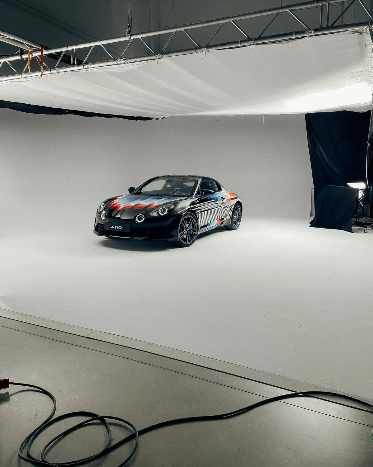 A black sports car with a colorful racing stripe pattern on a photo studio backdrop.