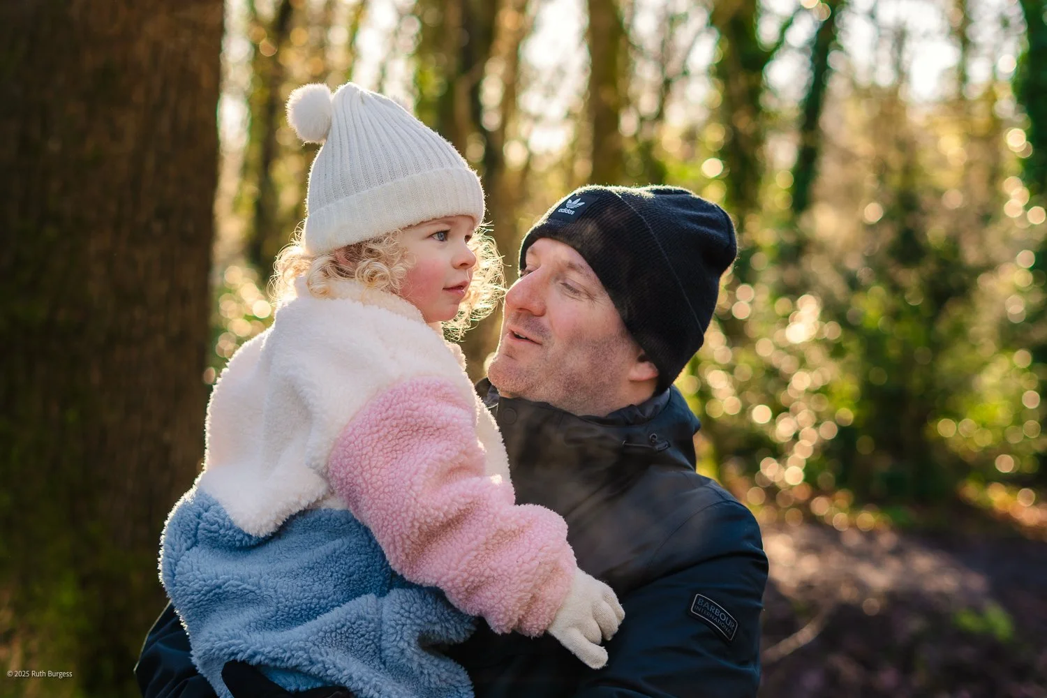 A man holding a young girl in a forest with sunlight filtering through trees.