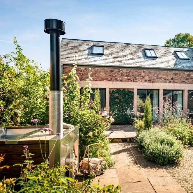 Landscaped garden with stone path and outdoor chimney beside a brick house, showing the kind of setting suited to a Tubmarine wood-fired hot tub.