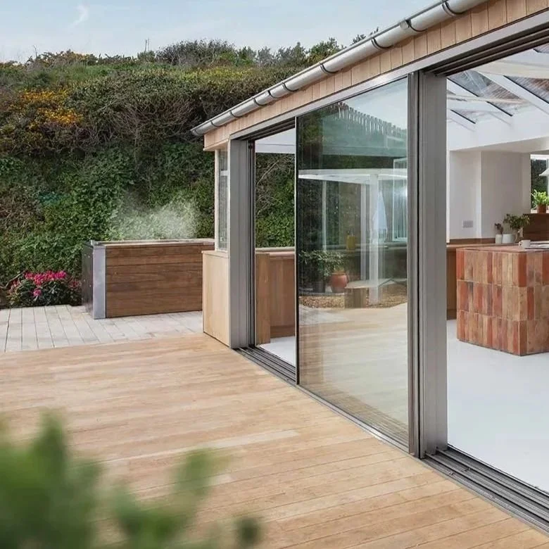 Modern house with large glass sliding doors, wooden deck, and interior featuring a kitchen with a brick island and a dining area with a wooden table and pendant lighting.
