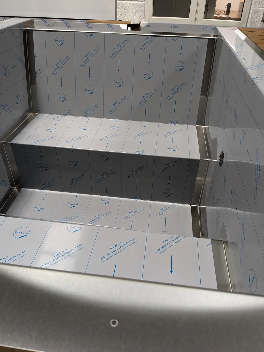 A formed stainless seat and backrest, still under protective film.