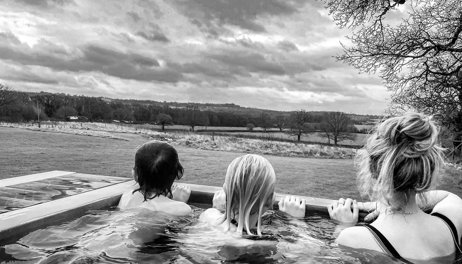 People relaxing in a Tubmarine wood-fired hot tub, looking out over open countryside.