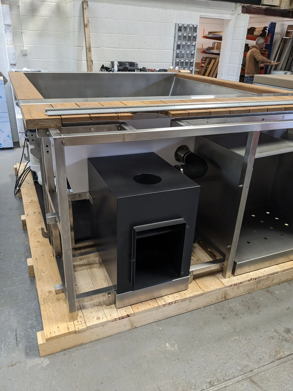 A stainless tub with timber trim, a maker working on wood behind it.