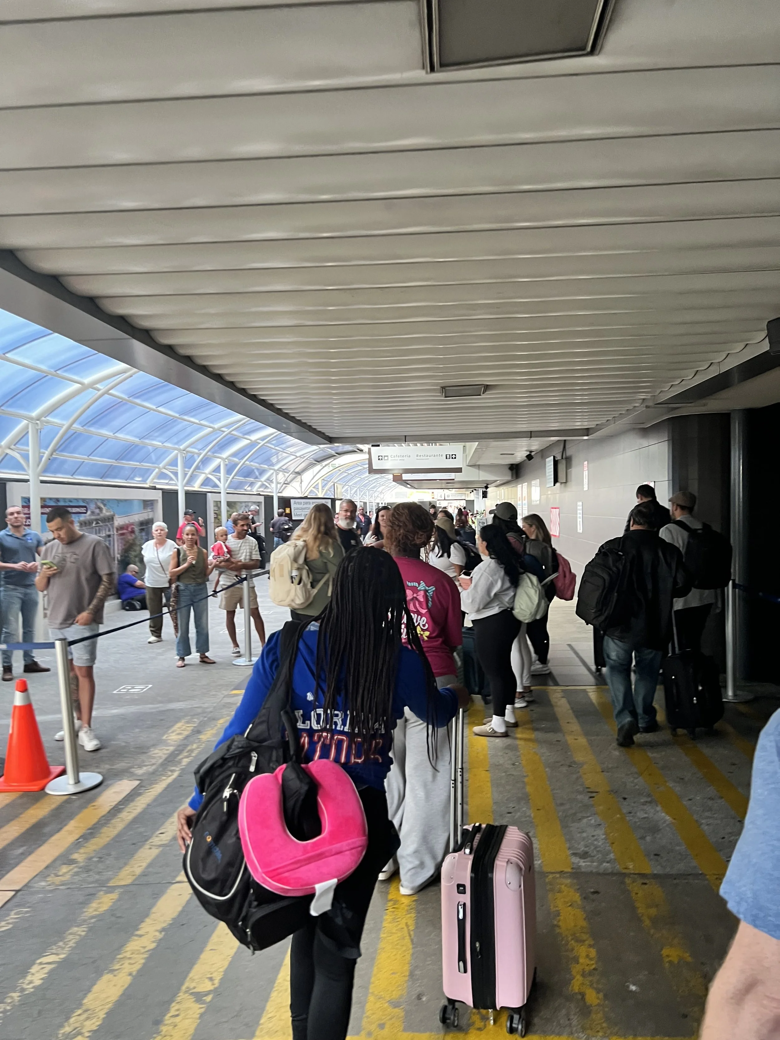 People waiting in line at the airport terminal with luggage and backpacks.