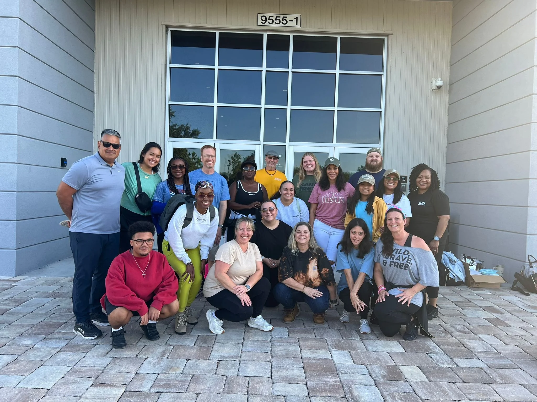 Group of diverse people standing and kneeling outside a building with large windows, posing for a photo.