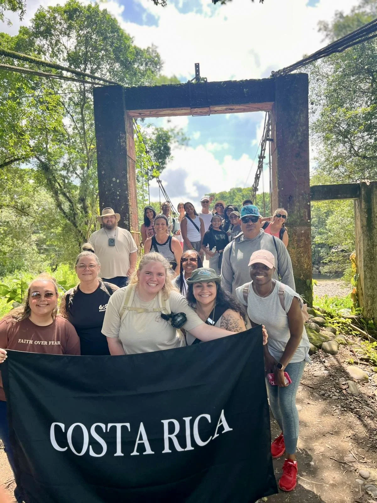 A group of people hiking in nature in Costa Rica, holding a black banner with white letters that read 'Costa Rica'.