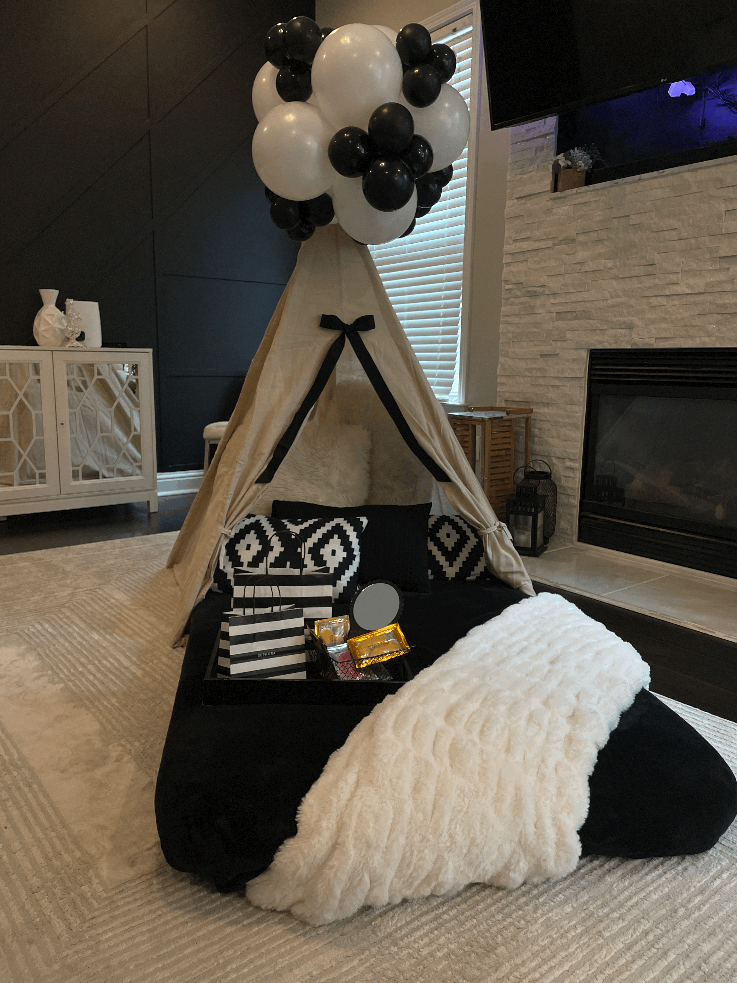 Choose a Sephora / makeup setup with a black and white color theme featuring a tent decorated with black and white balloons, black and white patterned cushions, a fluffy white throw, and gift bags and boxes as decor accents.